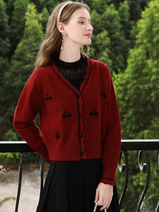Woman in embroidered red cardigan with hands folded, standing outdoors.