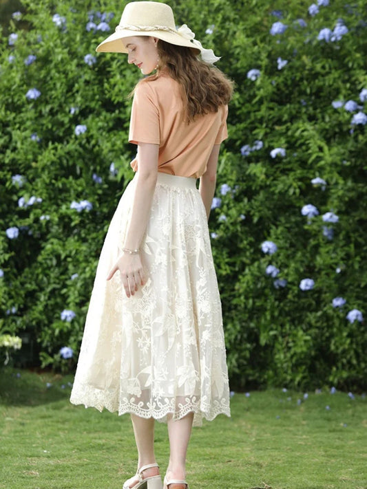Back view of woman in peach top and ivory lace skirt walking on grass near flowers.
