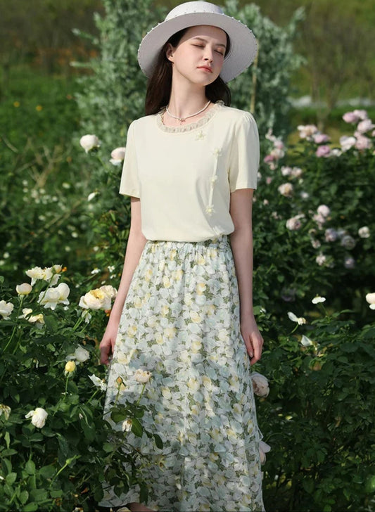 Side view of woman in yellow top and printed skirt standing in a field with hands in pockets.