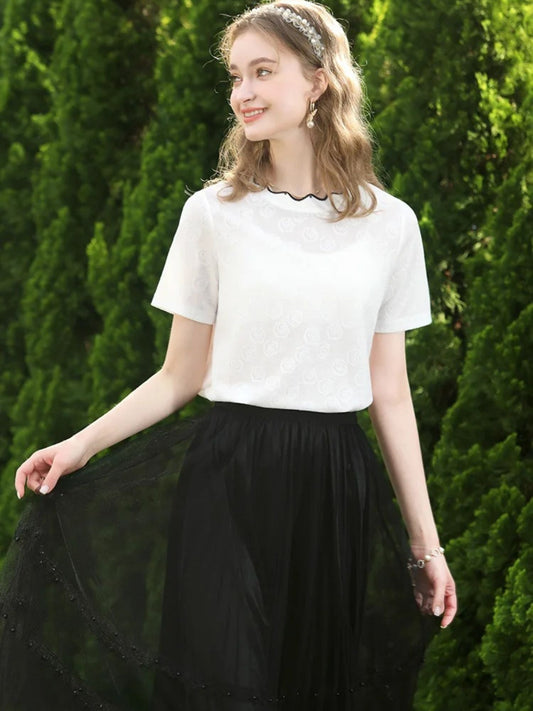 Woman in white blouse and black tulle skirt standing on grass, holding the skirt side.