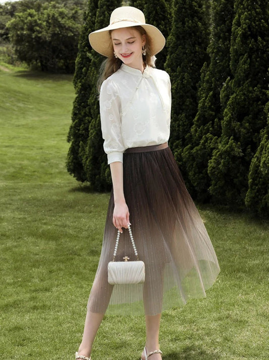 Woman in ombre mesh skirt and white blouse walking outdoors, holding a white handbag.