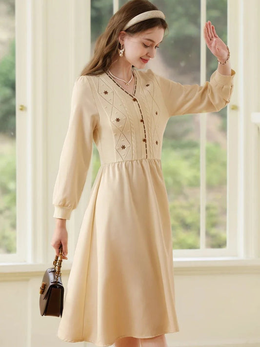 Woman in beige dress walking forward, holding a dark purse in one hand.