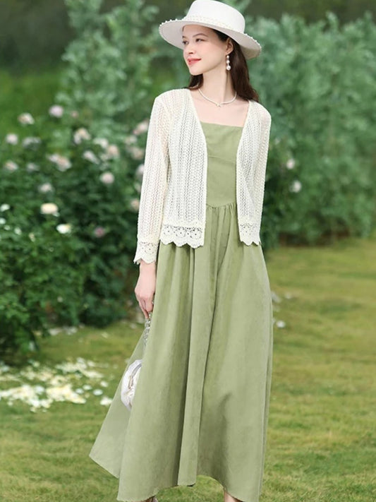 Woman in white open-knit cardigan over a green dress, walking in a flower garden.