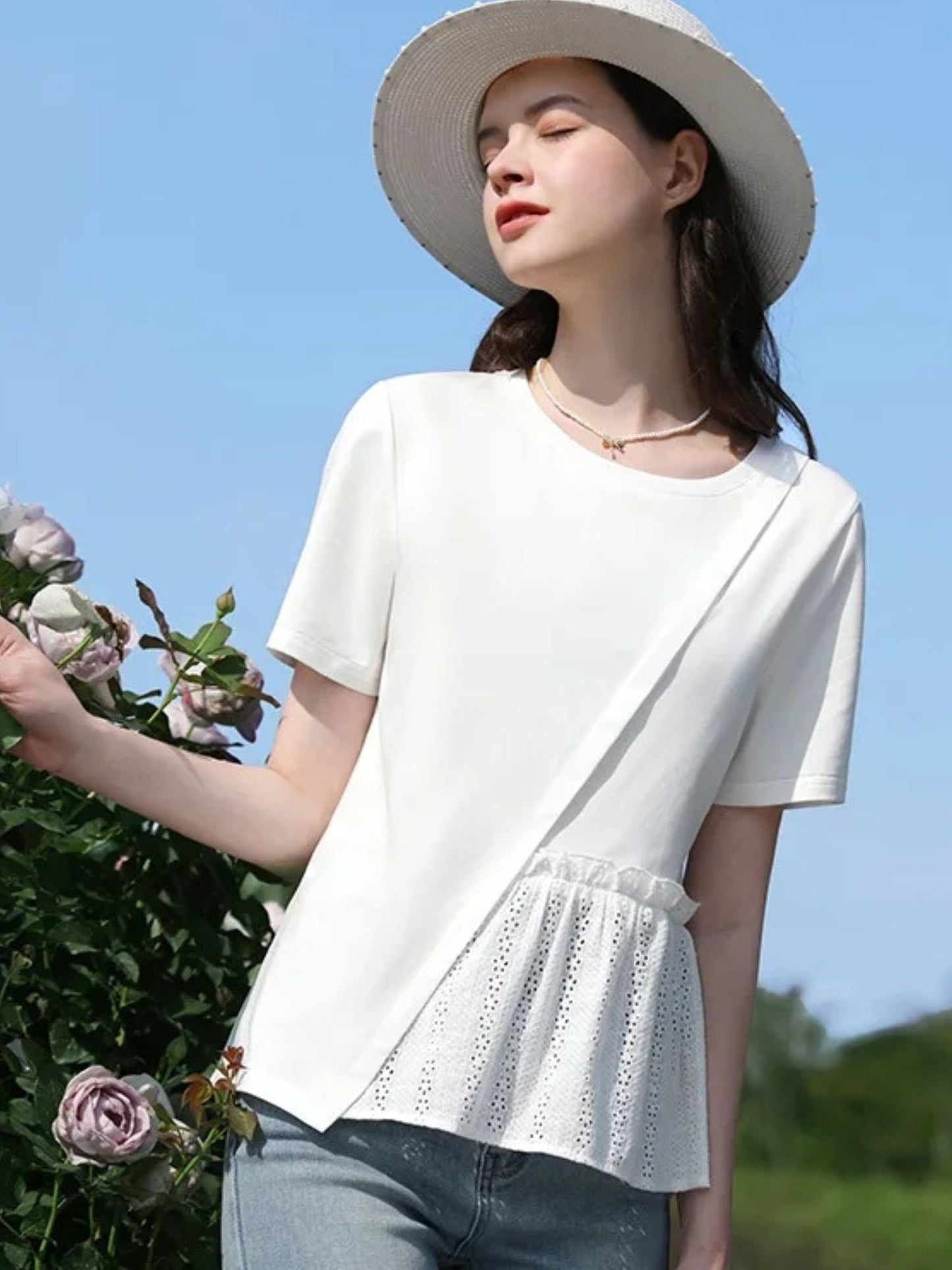 Woman in peplum blouse and jeans posing outdoors with hand on hip and eyes closed.