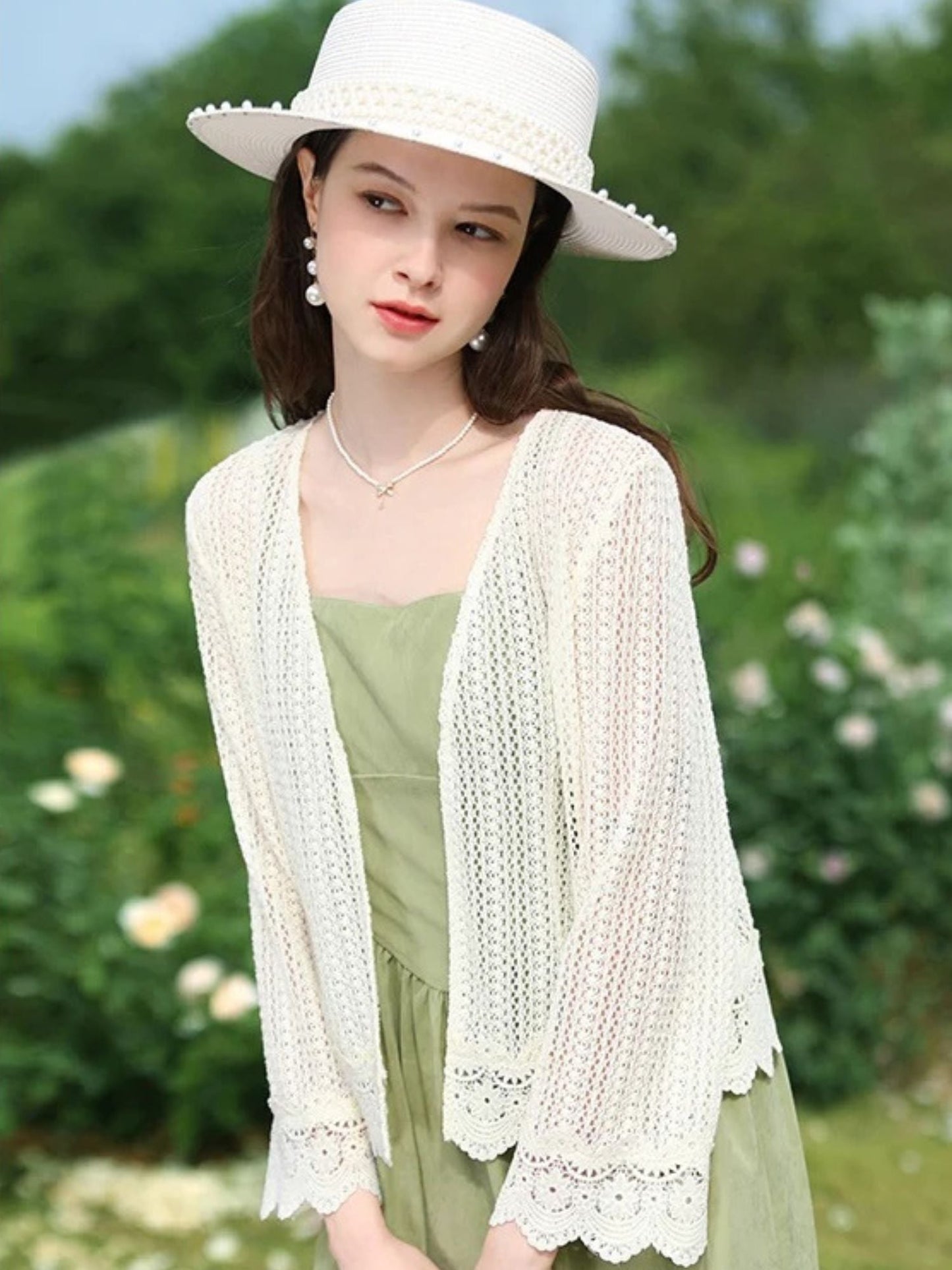 Woman in white crochet cardigan over sleeveless dress, facing forward with relaxed pose.