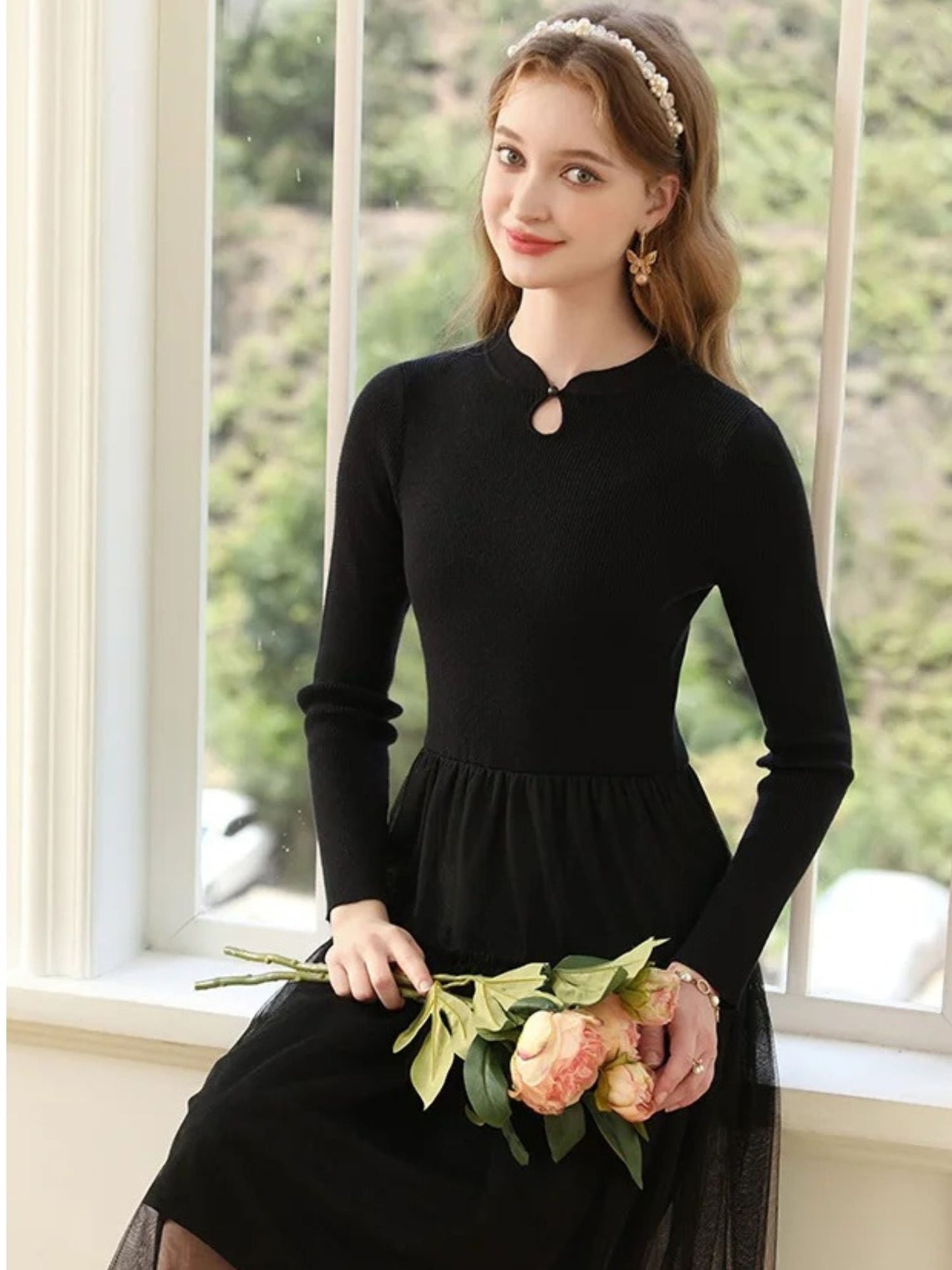 Woman in black dress smiling while holding a bouquet of pink flowers.