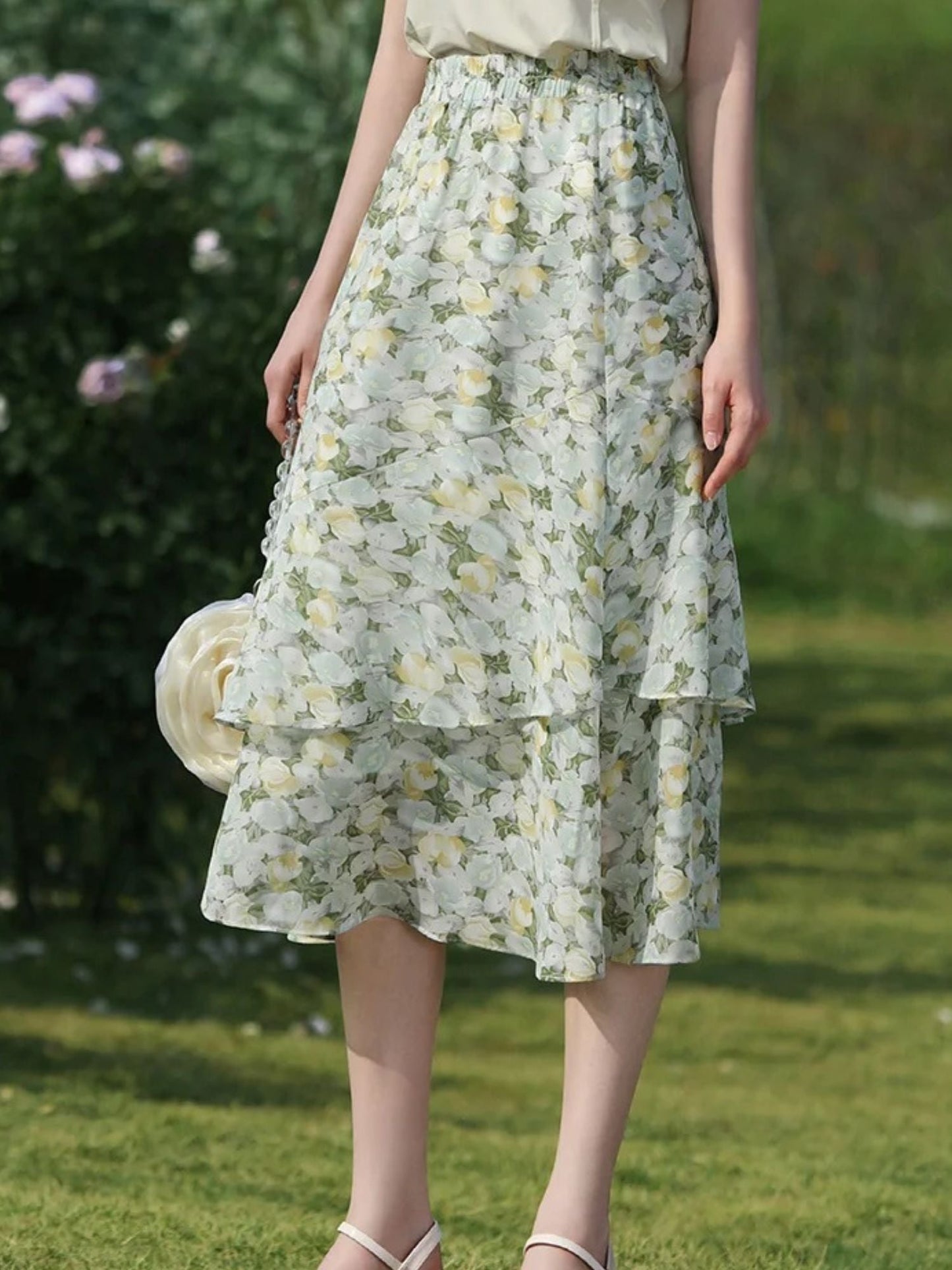Close-up of floral tiered skirt with small handbag, captured in natural sunlight.