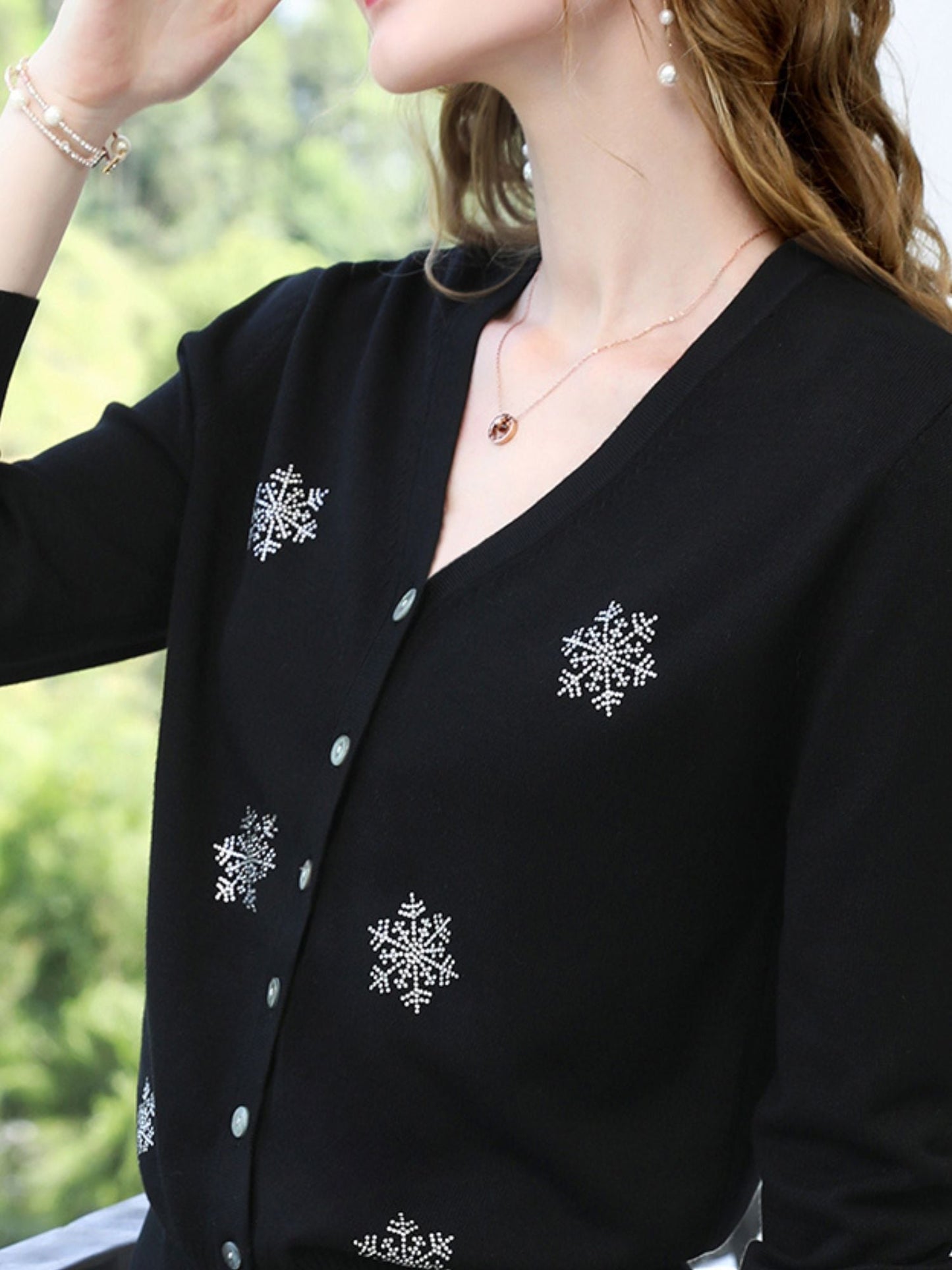Close-up of black cardigan with embroidered snowflake patterns and pearl-like buttons.