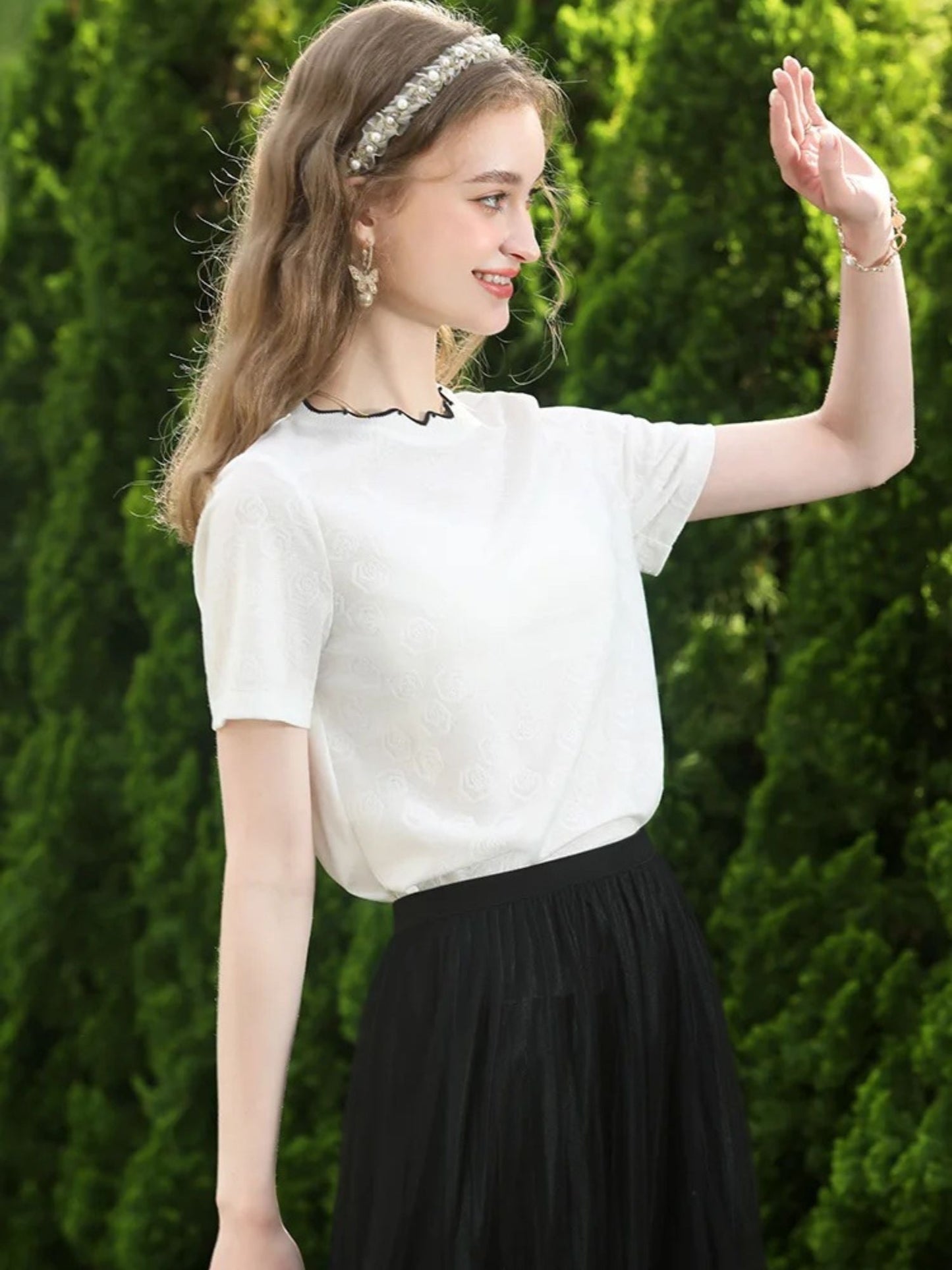 Close-up of white embroidered top with scalloped neckline and gold earrings.