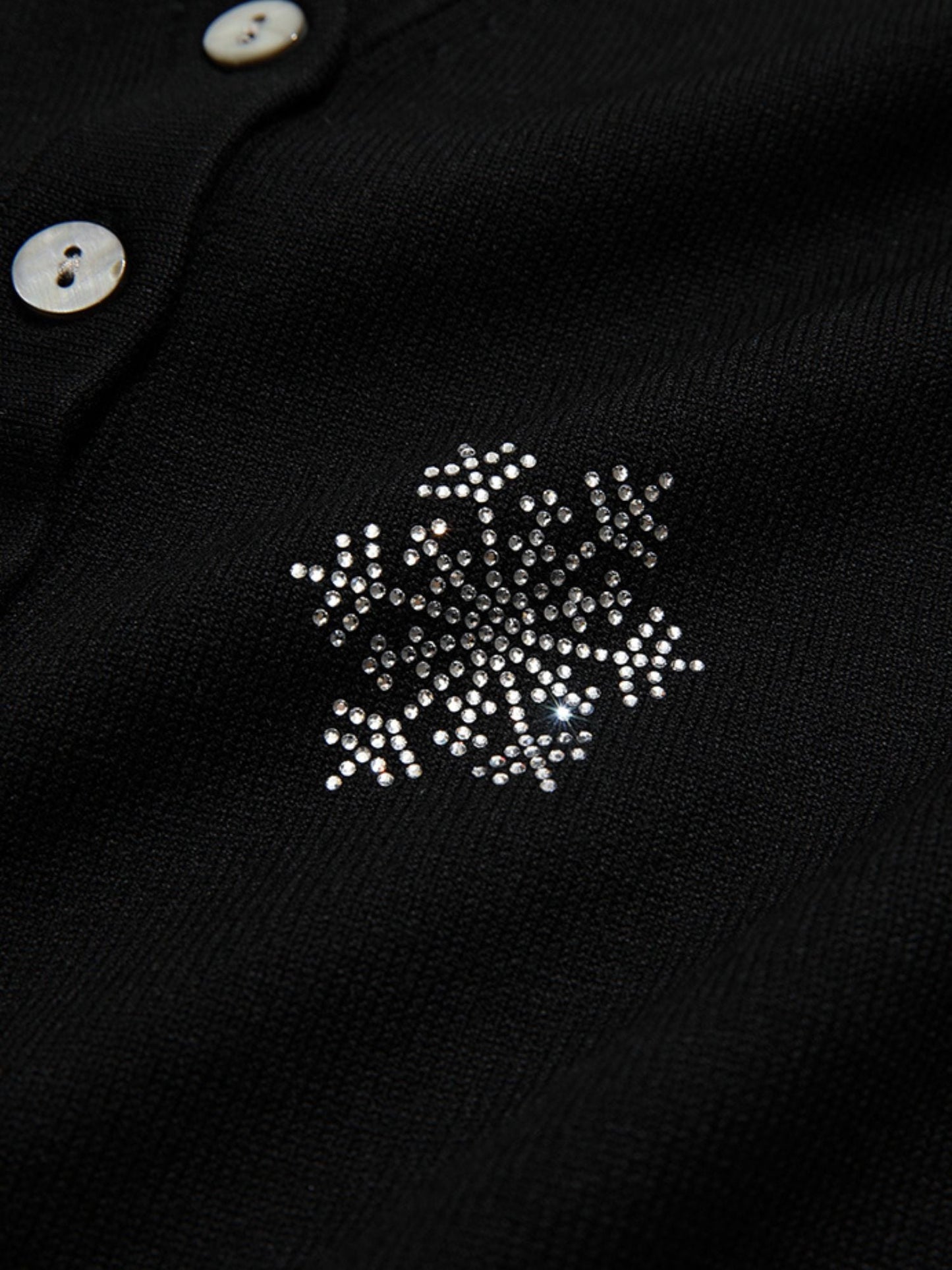 Detail view of snowflake embroidery on the upper chest of a black buttoned cardigan.