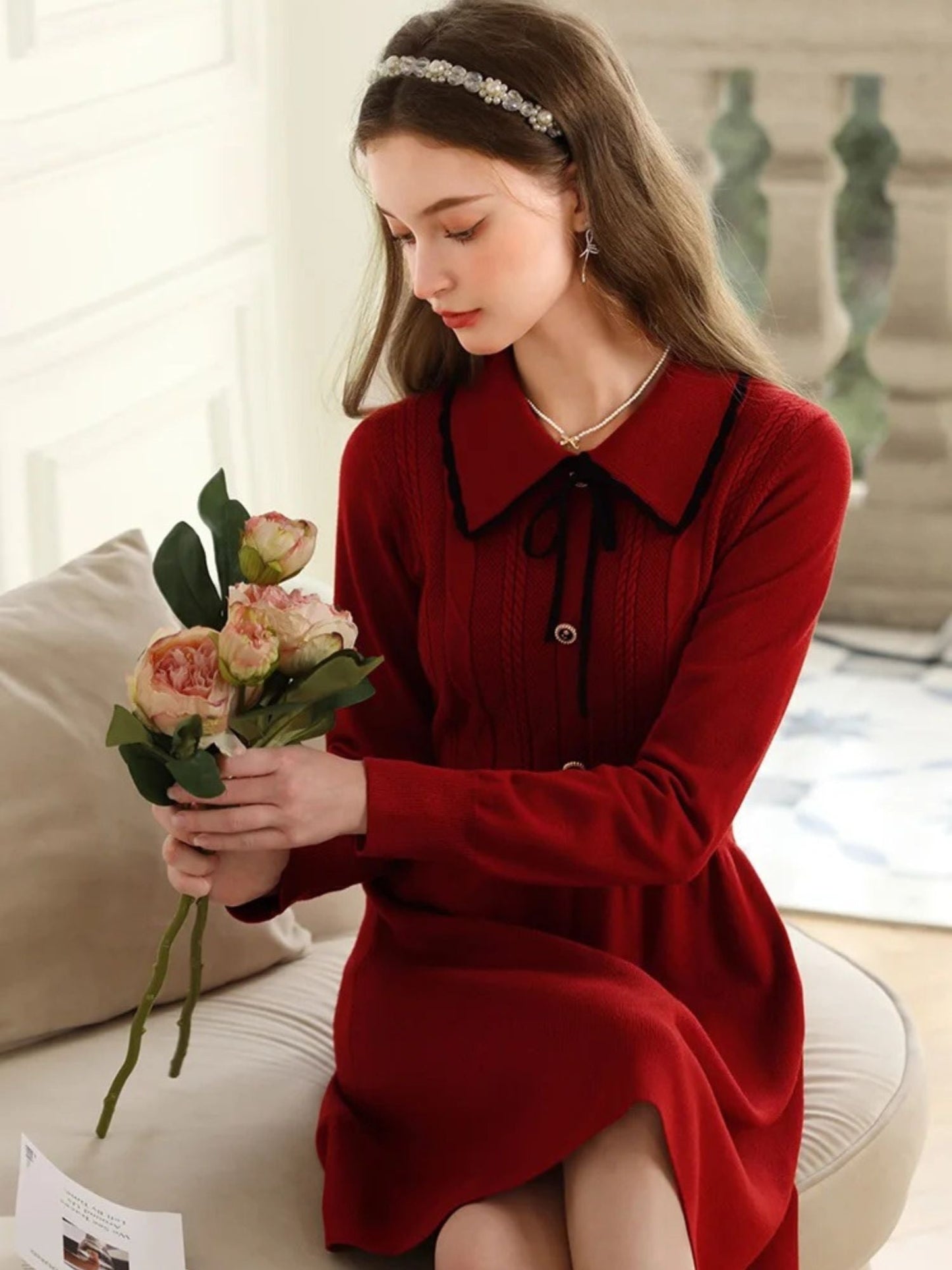 Seated woman in red dress holding a flower bouquet near a white balcony.