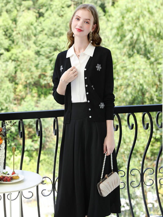 Woman in black cardigan with snowflake embroidery over a white top, holding a small quilted purse.
