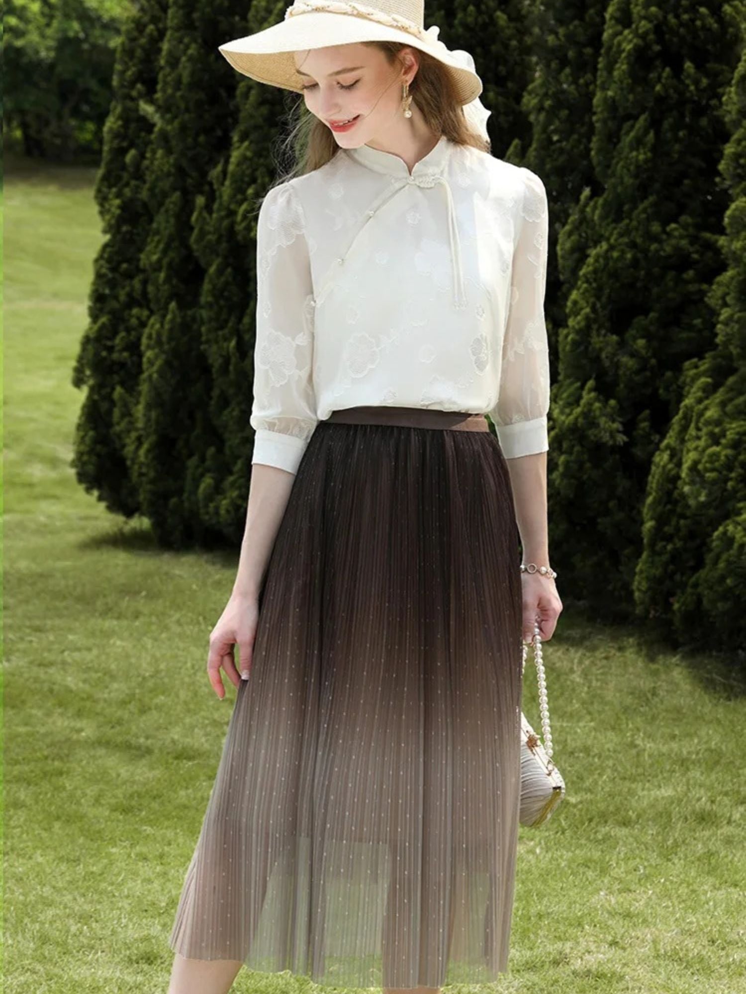 Woman in white floral blouse and ombre tulle midi skirt, smiling in a sunhat.