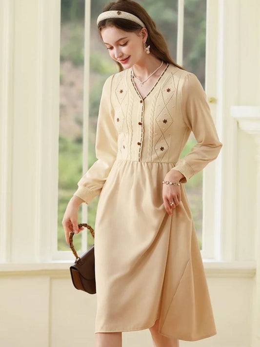 Woman in cream button-front dress with gathered waist, holding a brown handbag and smiling.