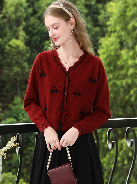 Woman in deep red cardigan with floral embroidery, holding a burgundy purse on a balcony.
