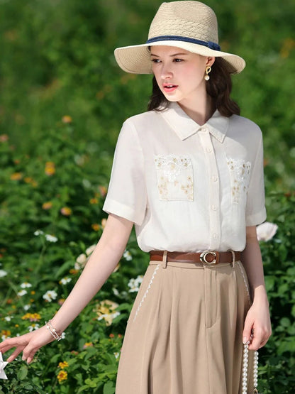 Woman in embroidered short-sleeve blouse and beige skirt with belt, wearing a straw hat outdoors.