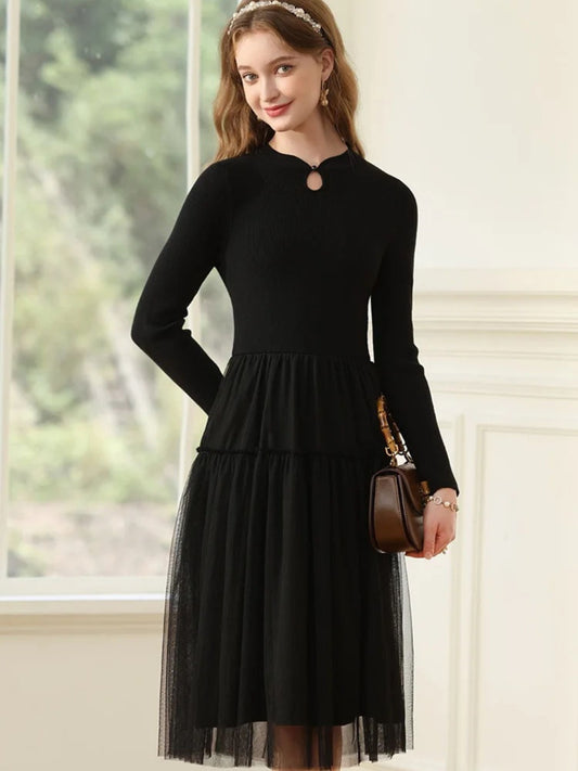 Woman in black long-sleeve dress with pleated mesh skirt and keyhole neckline, holding a brown handbag.
