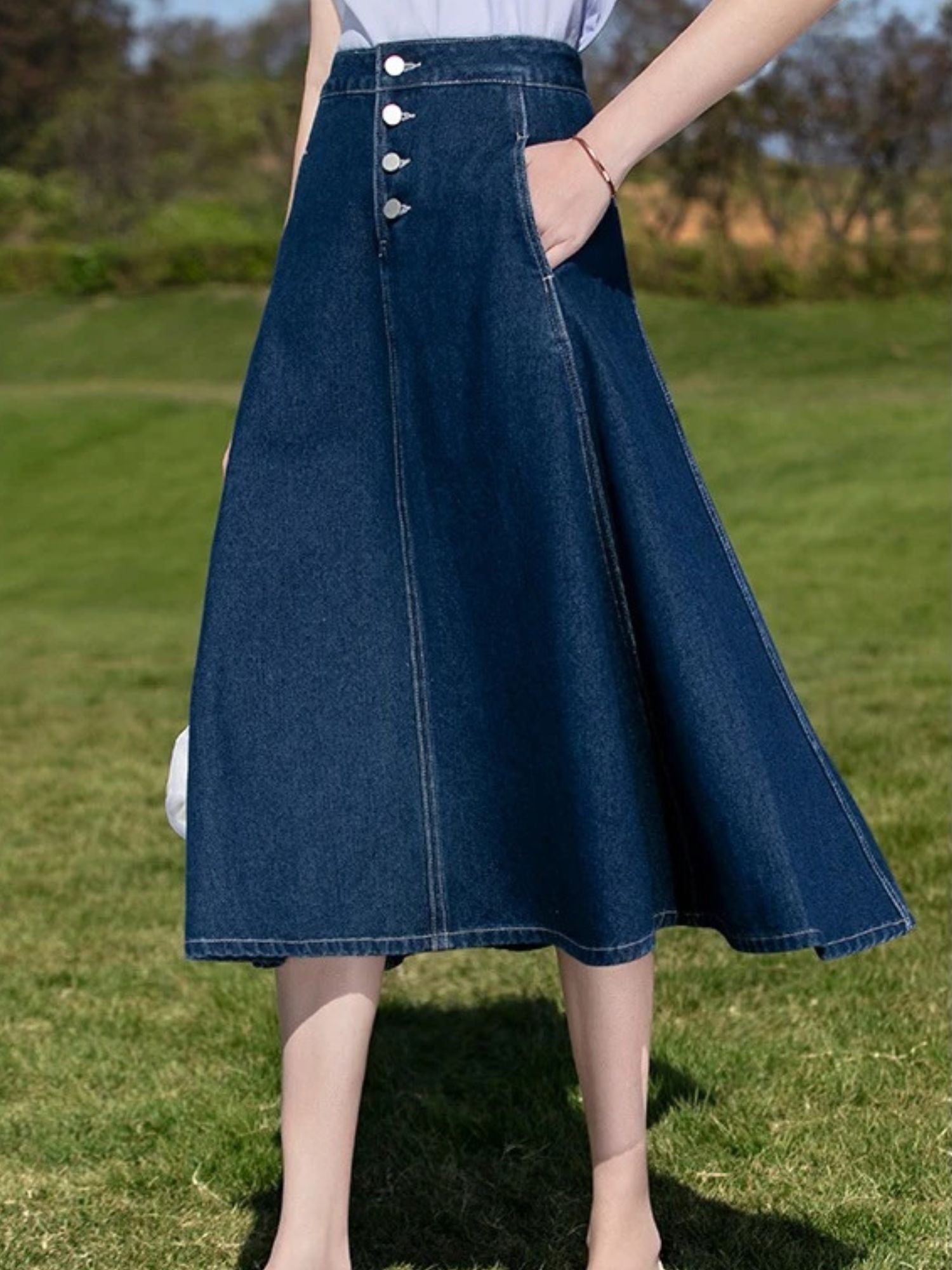 Close-up of flared dark blue denim skirt with front buttons and side pockets.