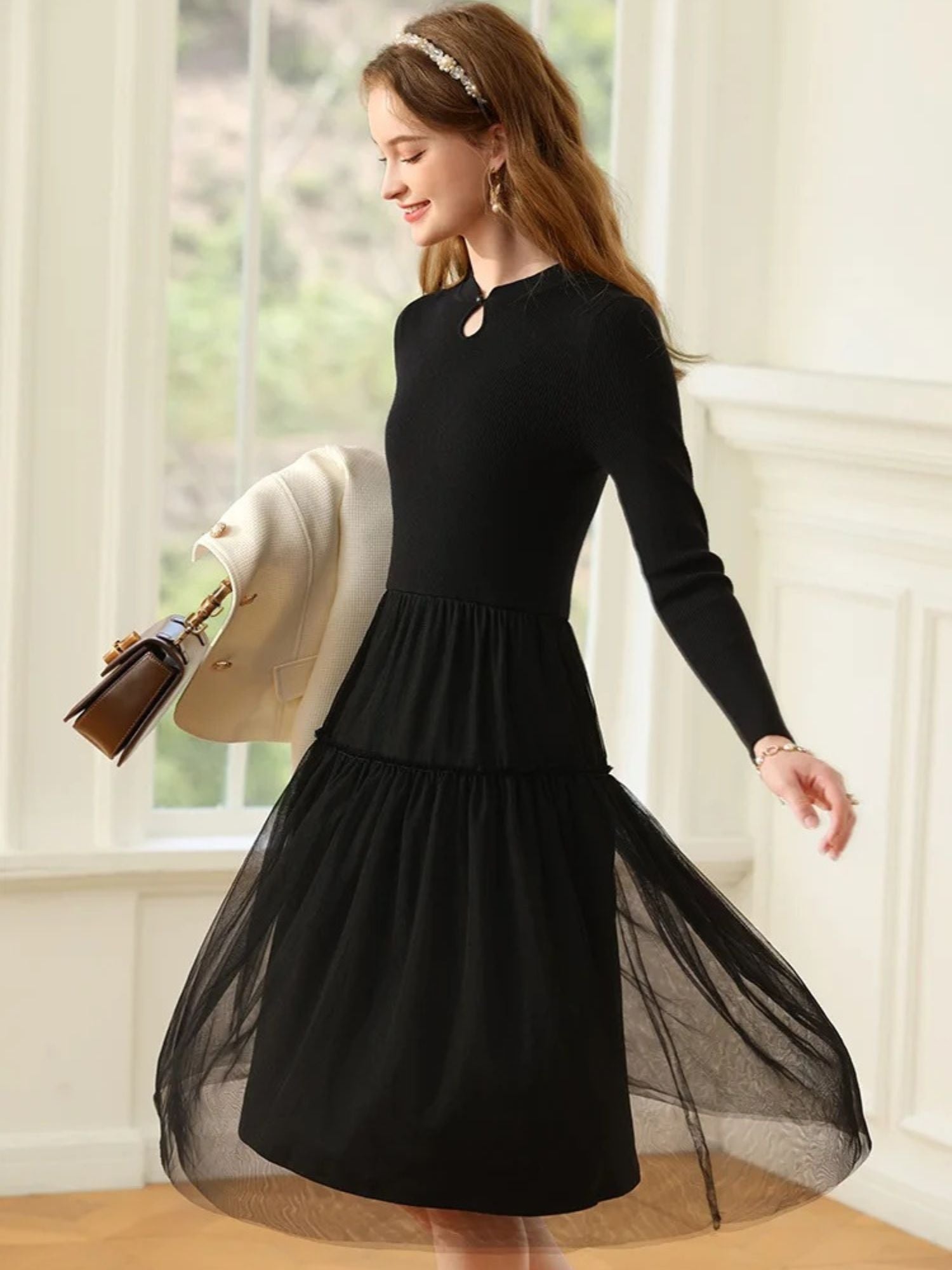 Woman twirling in black dress with sheer layered skirt, holding a black clutch.