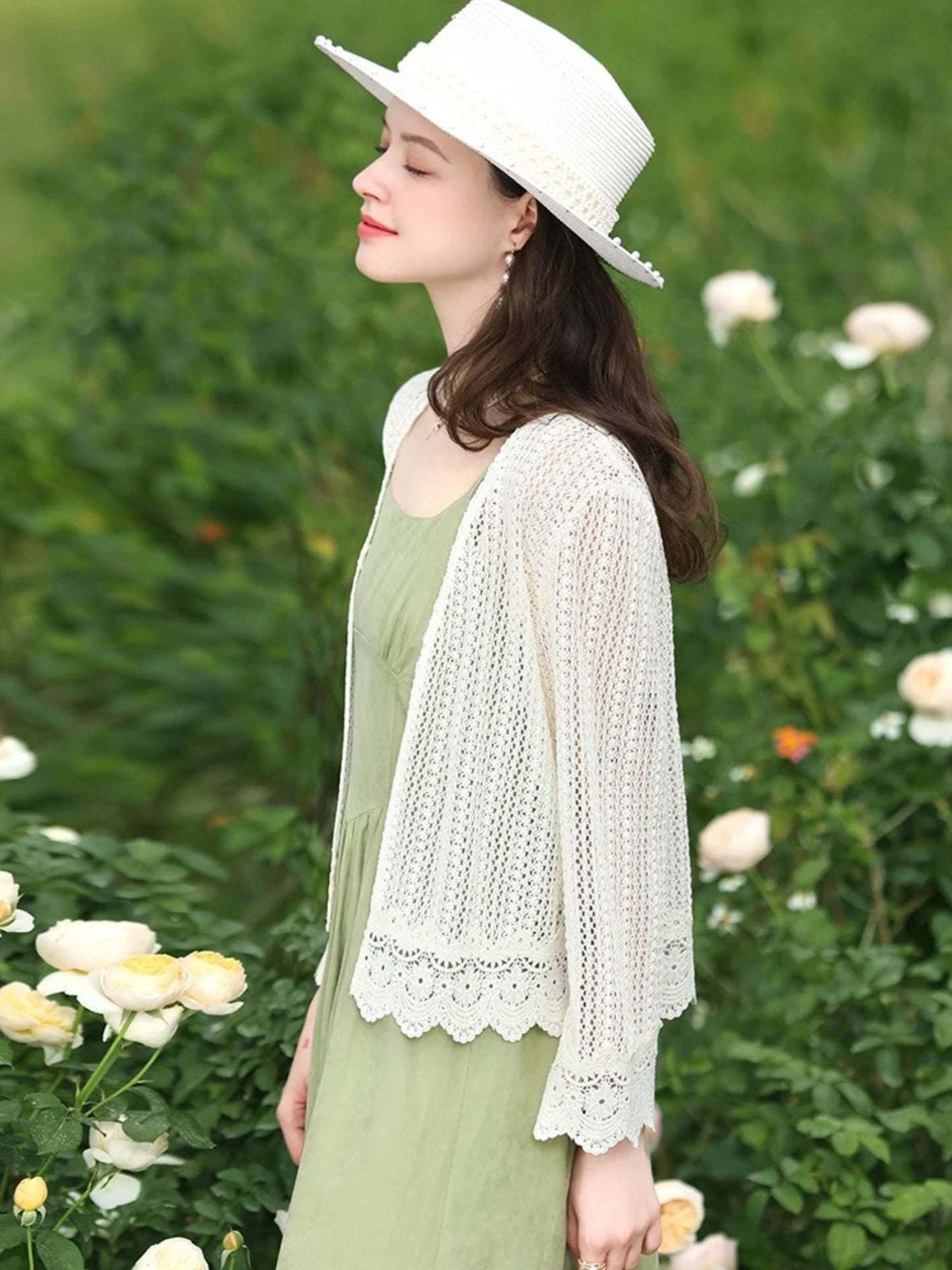 Side view of woman in white lace cardigan and sunhat, standing among white flowers.
