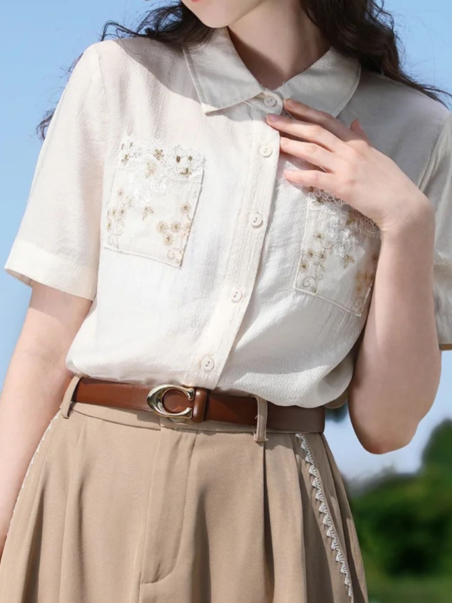 Close-up of embroidered shirt with pocket details, tucked into a belted skirt.