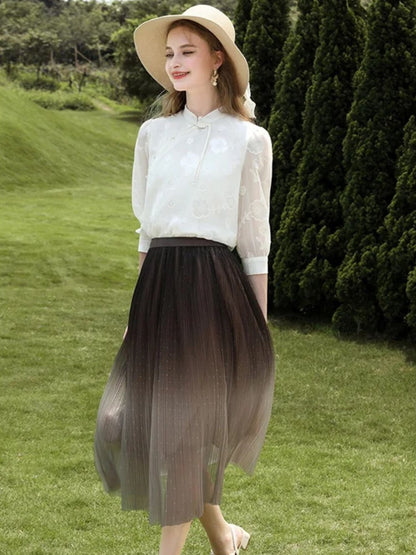 Woman in light blouse and flowing brown-to-beige skirt, smiling in the sun.