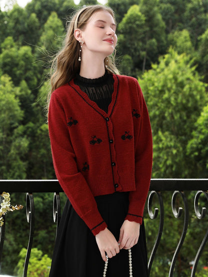 Woman in red floral knit cardigan smiling slightly, looking to the side on a balcony.
