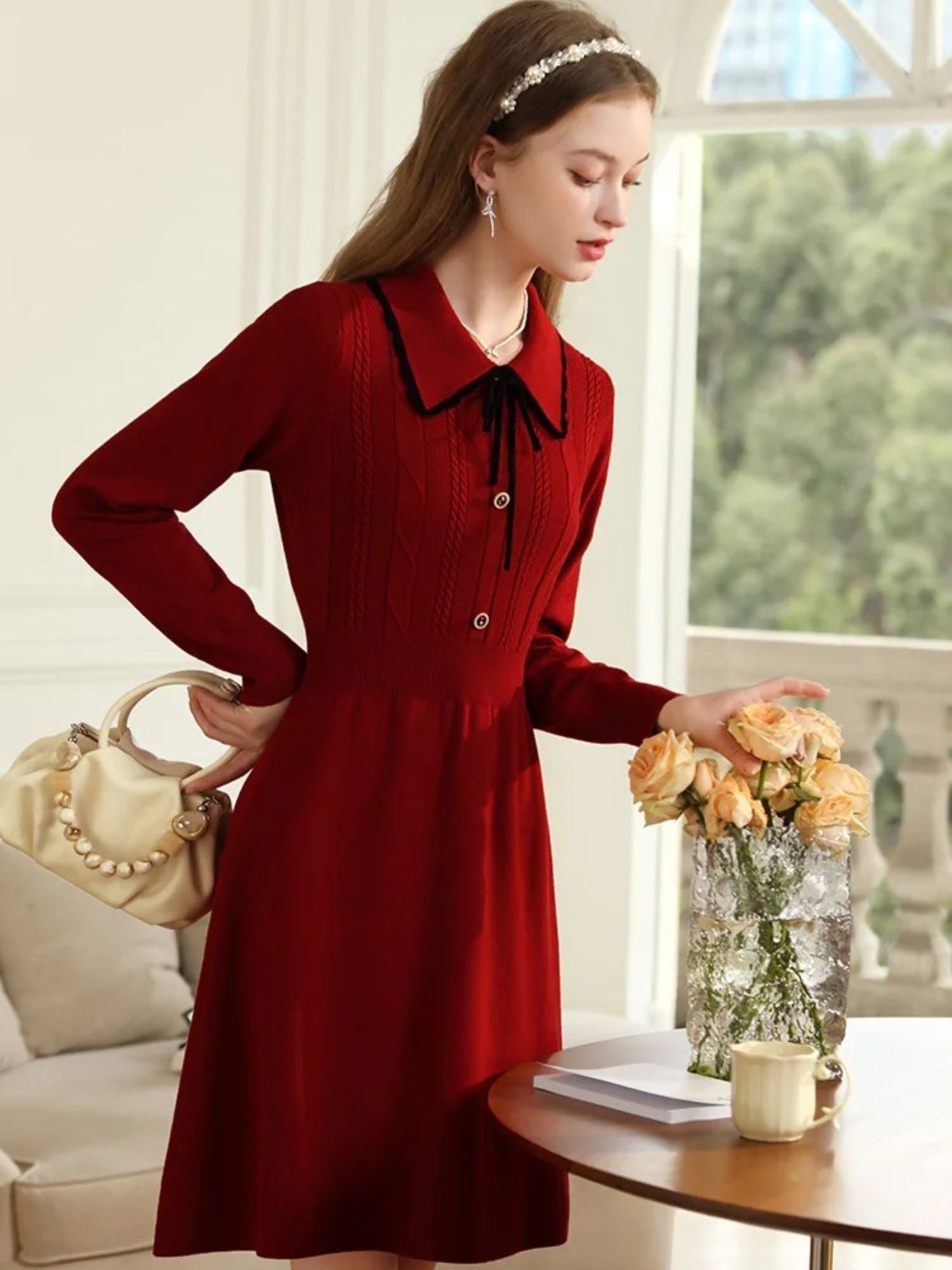 Woman in red dress standing with hands clasped next to a table with flowers.