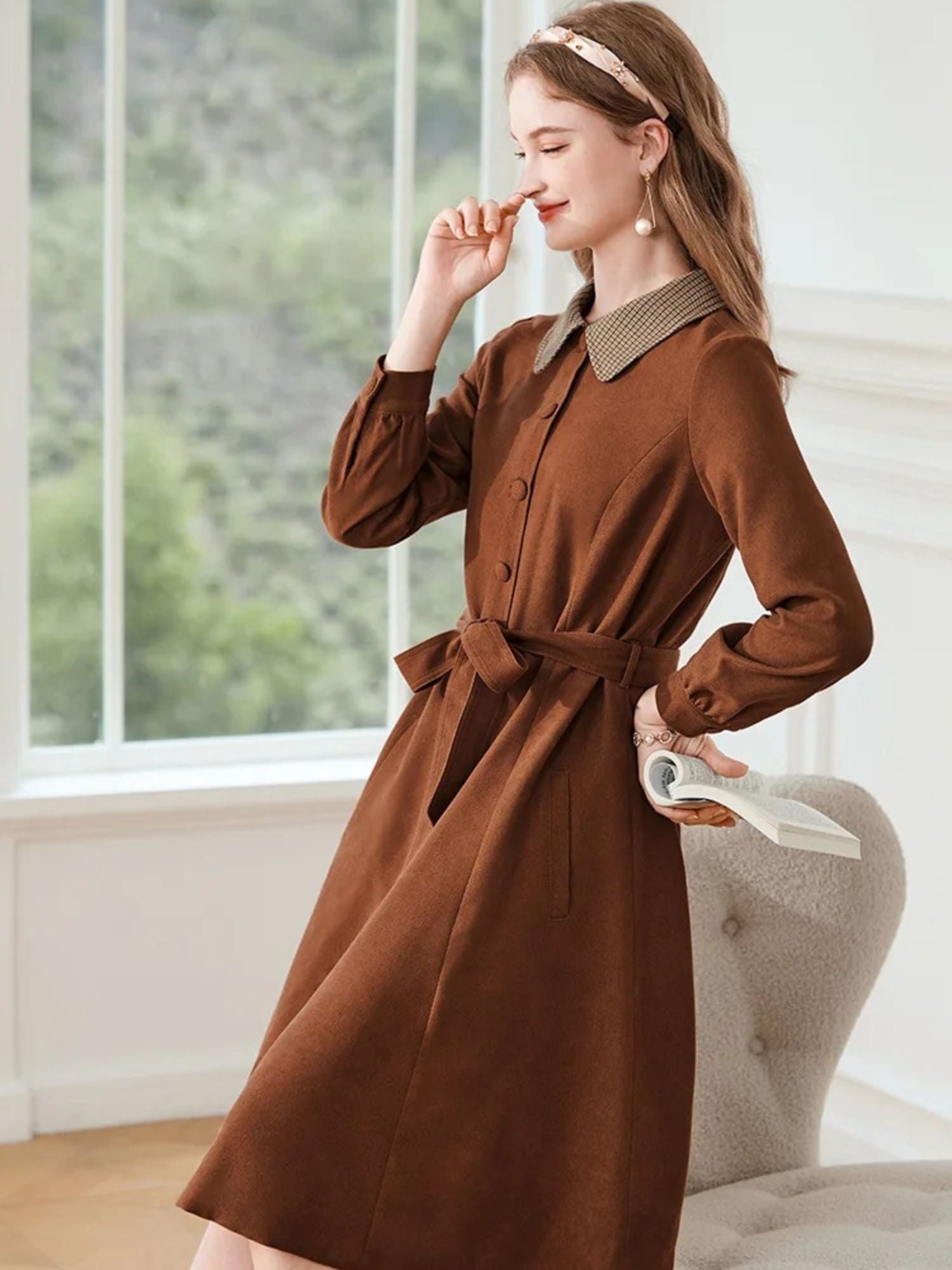 Woman in brown long-sleeve dress with checked collar, holding a small beige handbag.