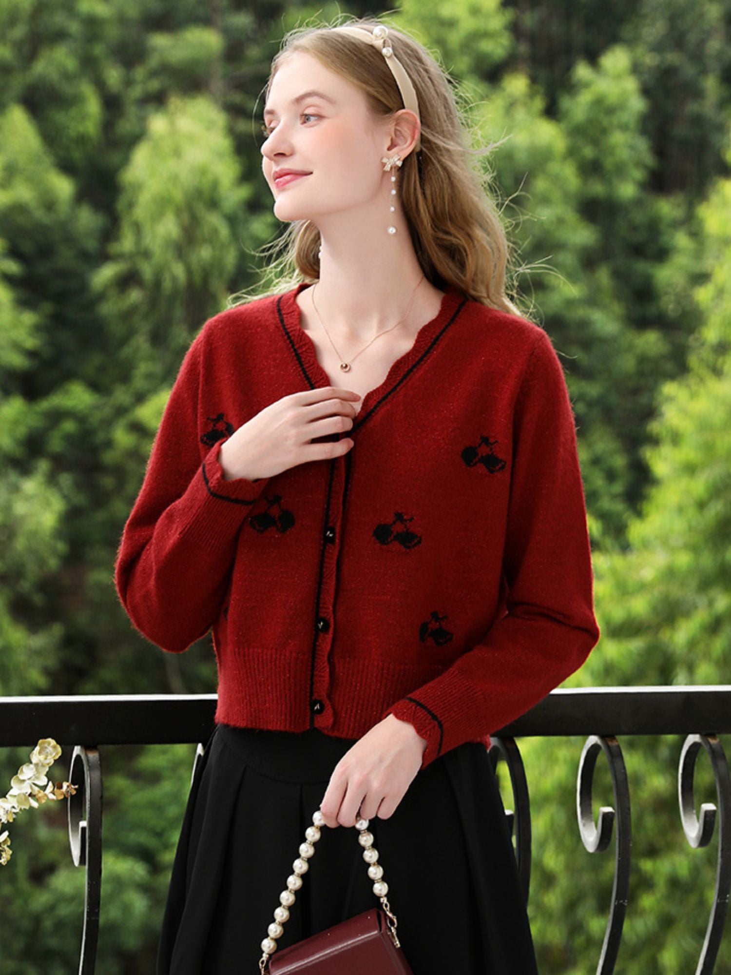 Woman gently touching her embroidered cardigan while holding a pearl handbag.