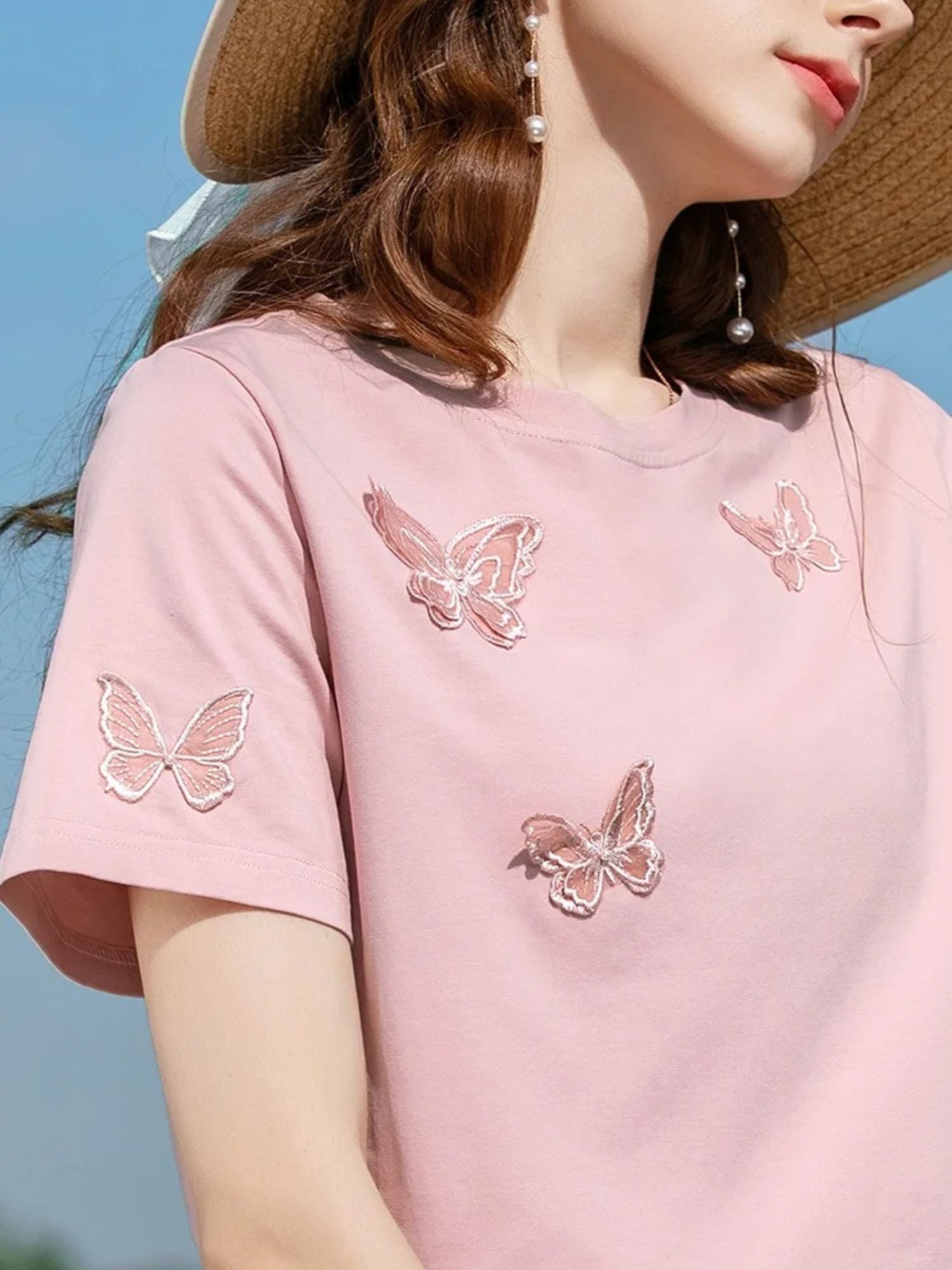 Close-up of pink t-shirt with butterfly embroidery on the chest and sleeve.