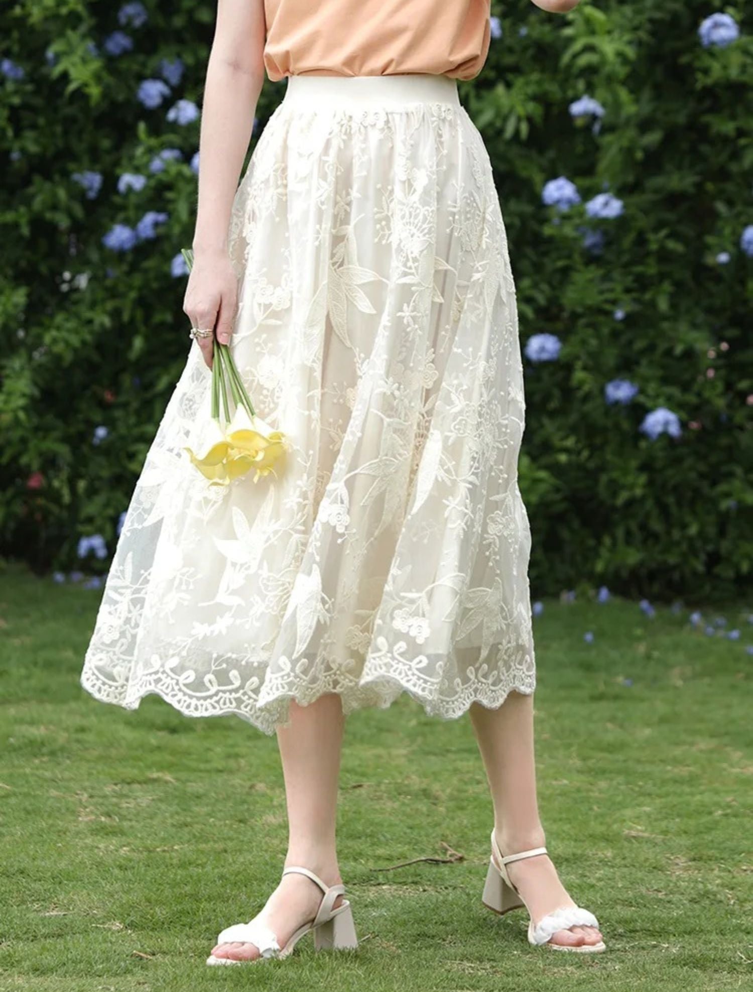 Close-up of lace skirt with scalloped hem and yellow flowers in hand.