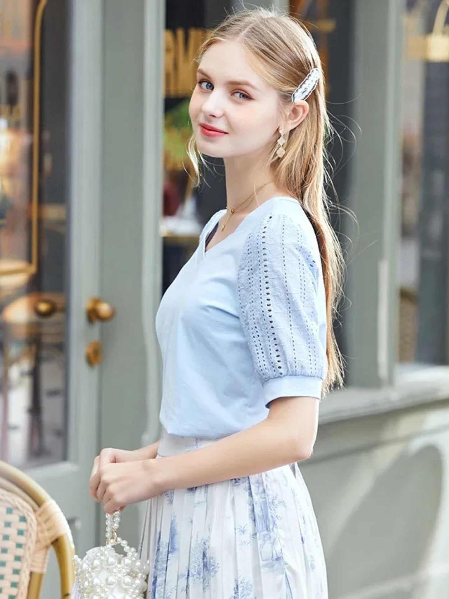 Woman in blue short-sleeve blouse smiling while standing outside a café.