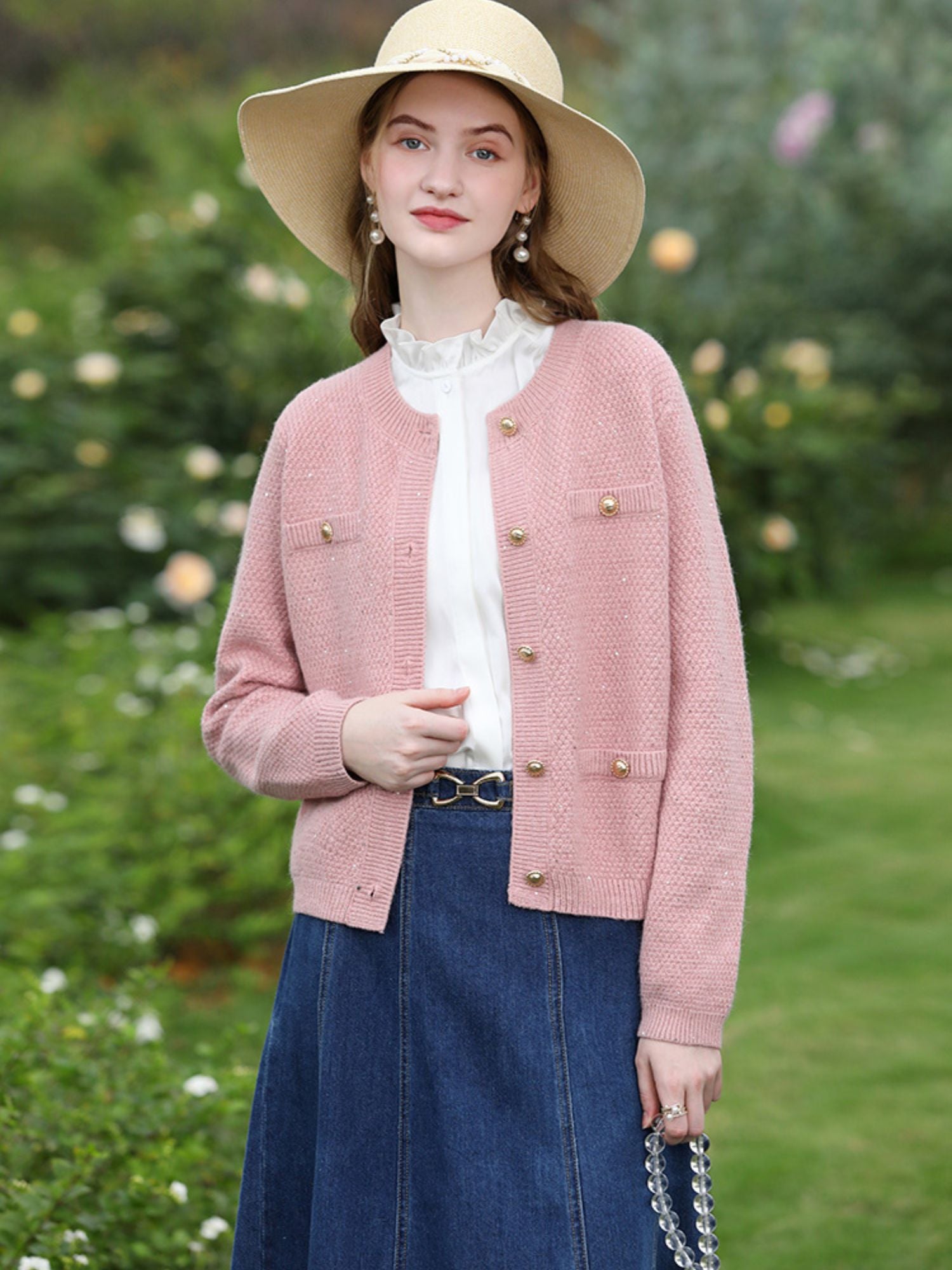 Woman in pink cardigan and white blouse paired with a denim skirt and straw hat.