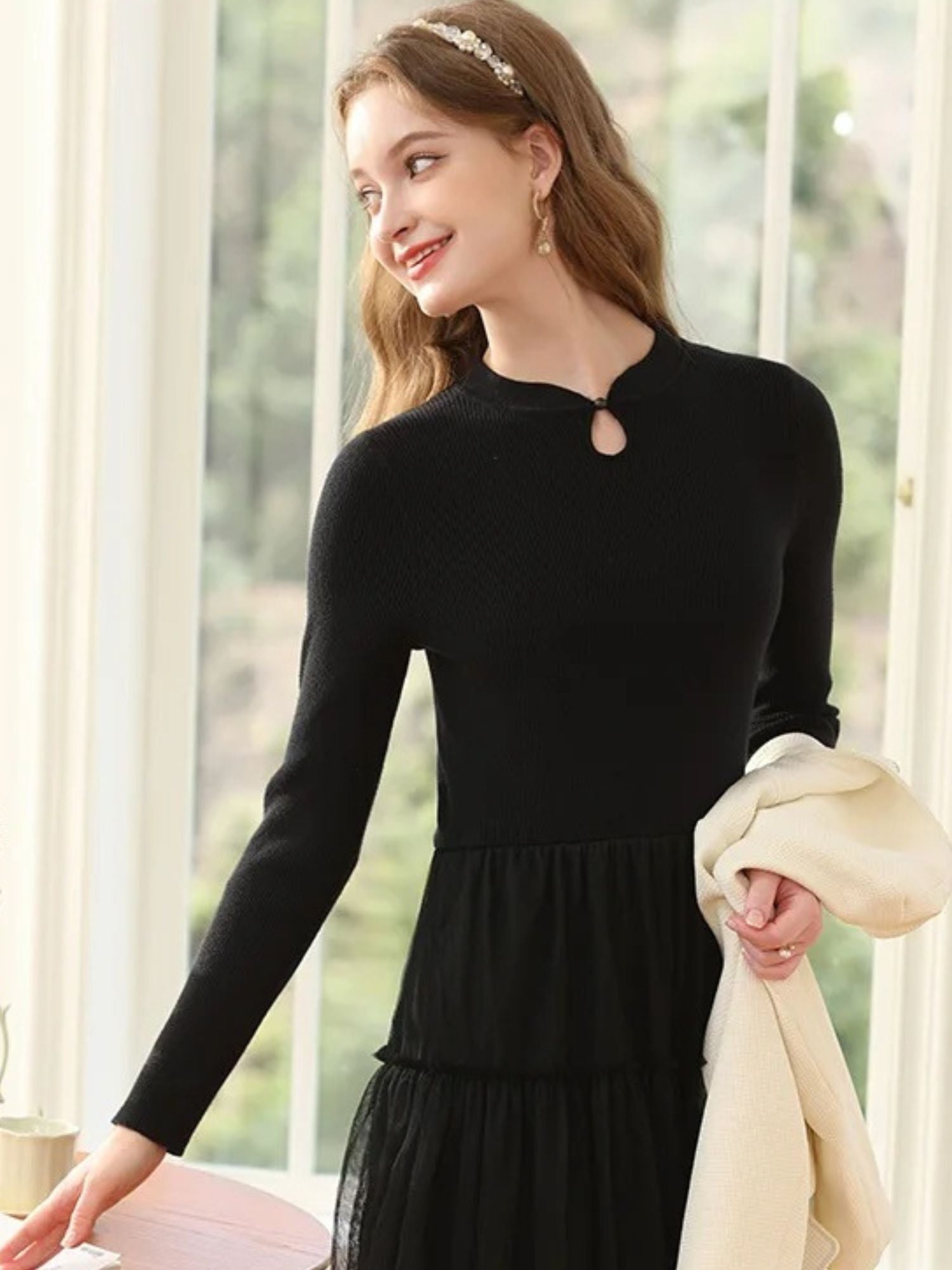 Side view of woman in black dress with pleated skirt, holding a white coat.