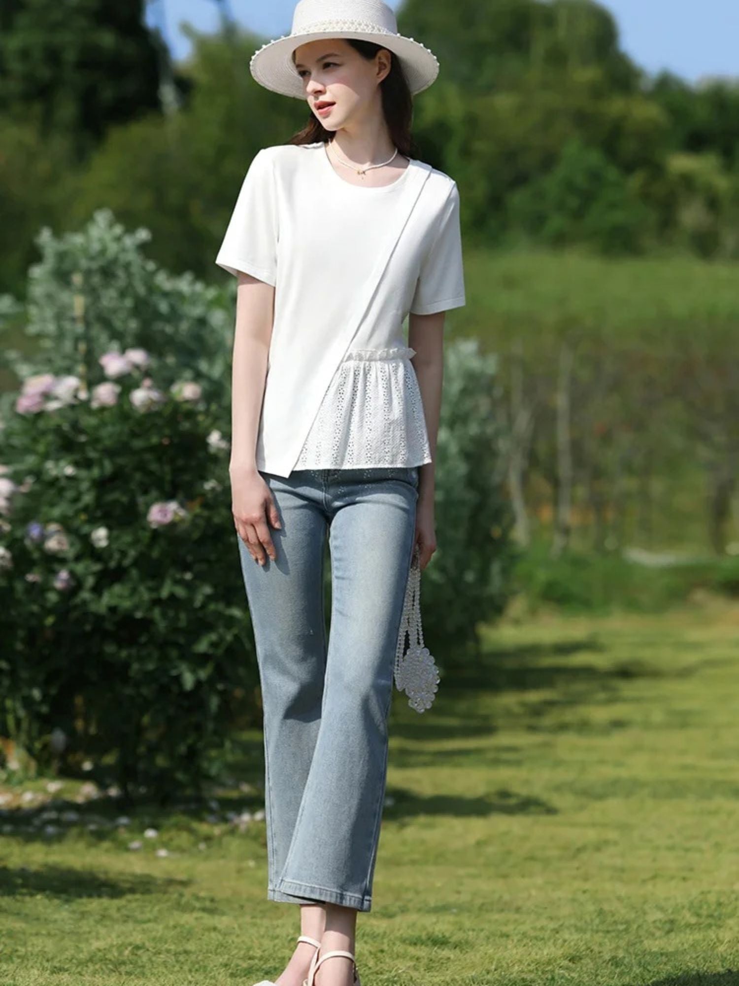 Woman in white top and cropped jeans standing on grass path in full-body view.

