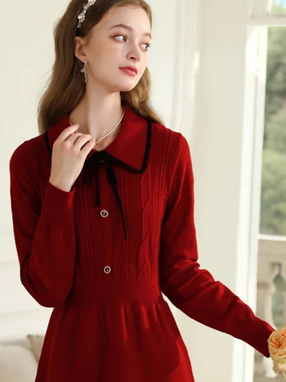 Woman in red knit dress with black collar smiling and touching her chin.