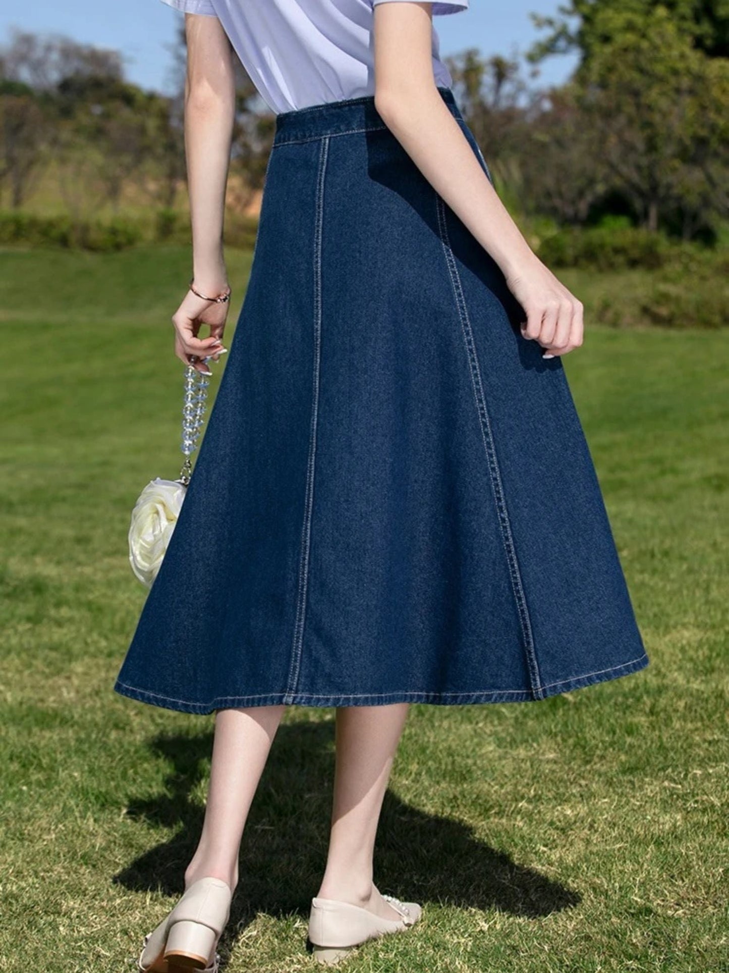Back view of woman in denim midi skirt and light top walking barefoot on grass.