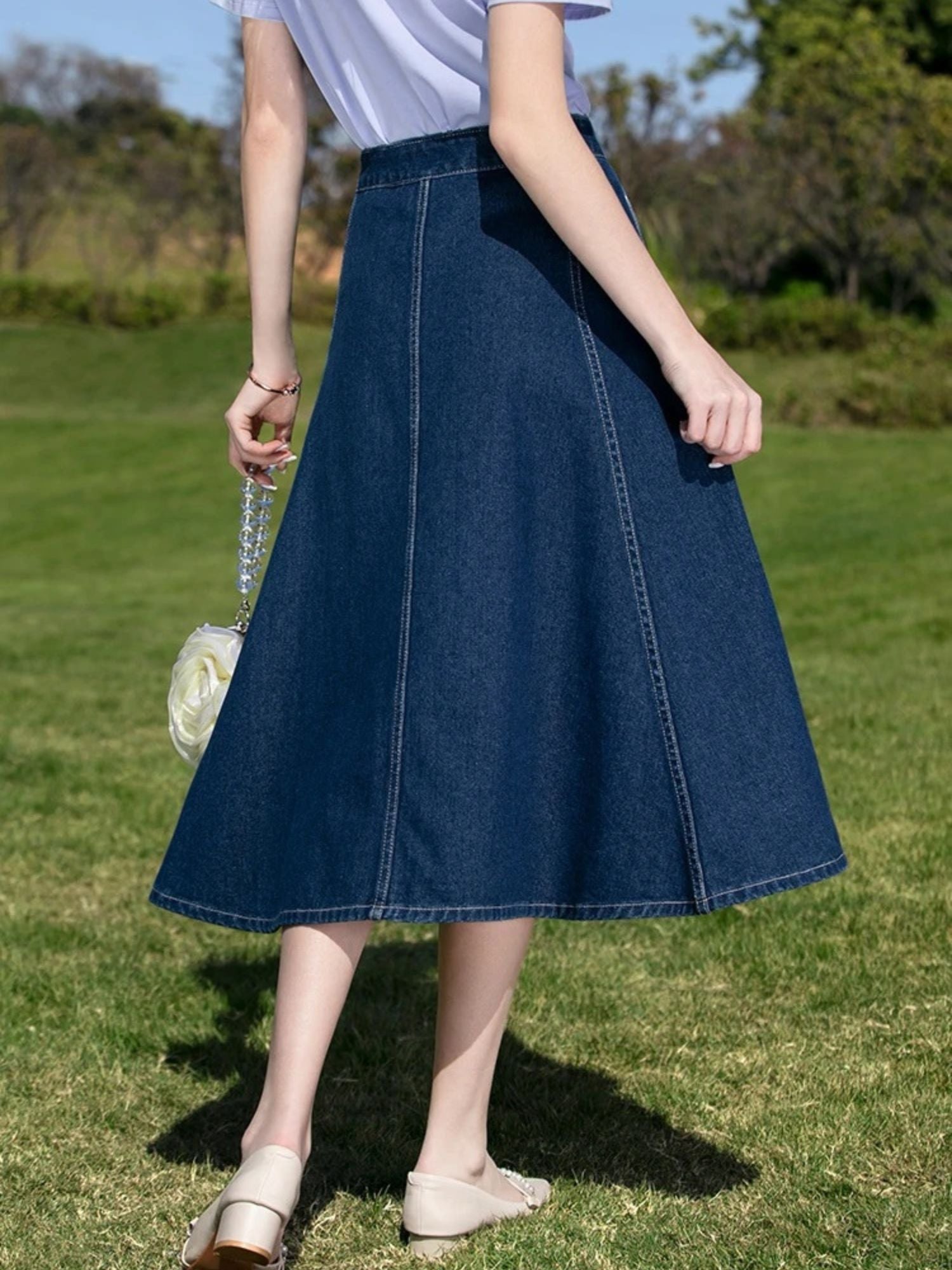 Back view of woman in denim midi skirt and light top walking barefoot on grass.