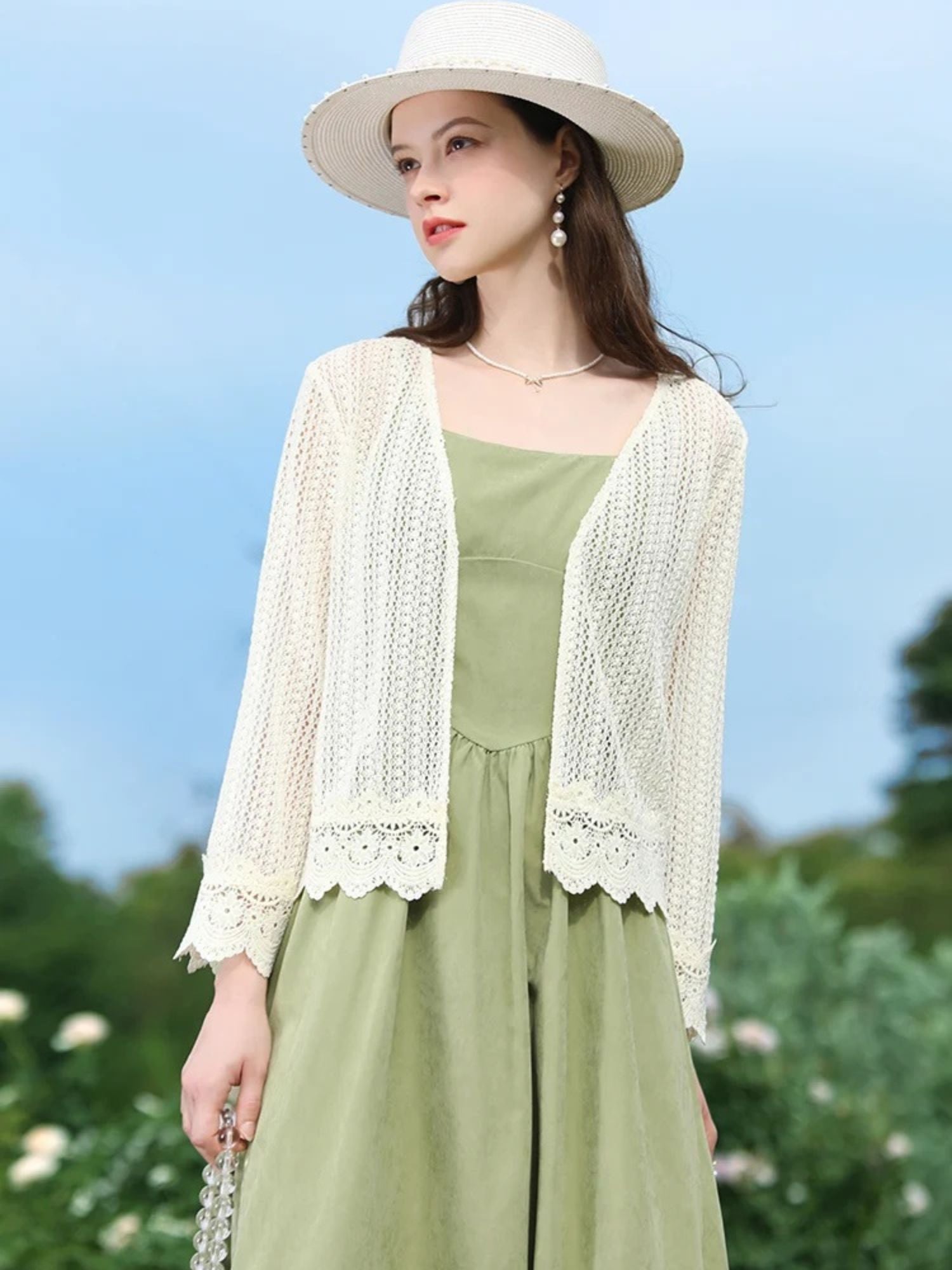 Side view of woman in open-knit cardigan and green dress, smiling under a clear sky.