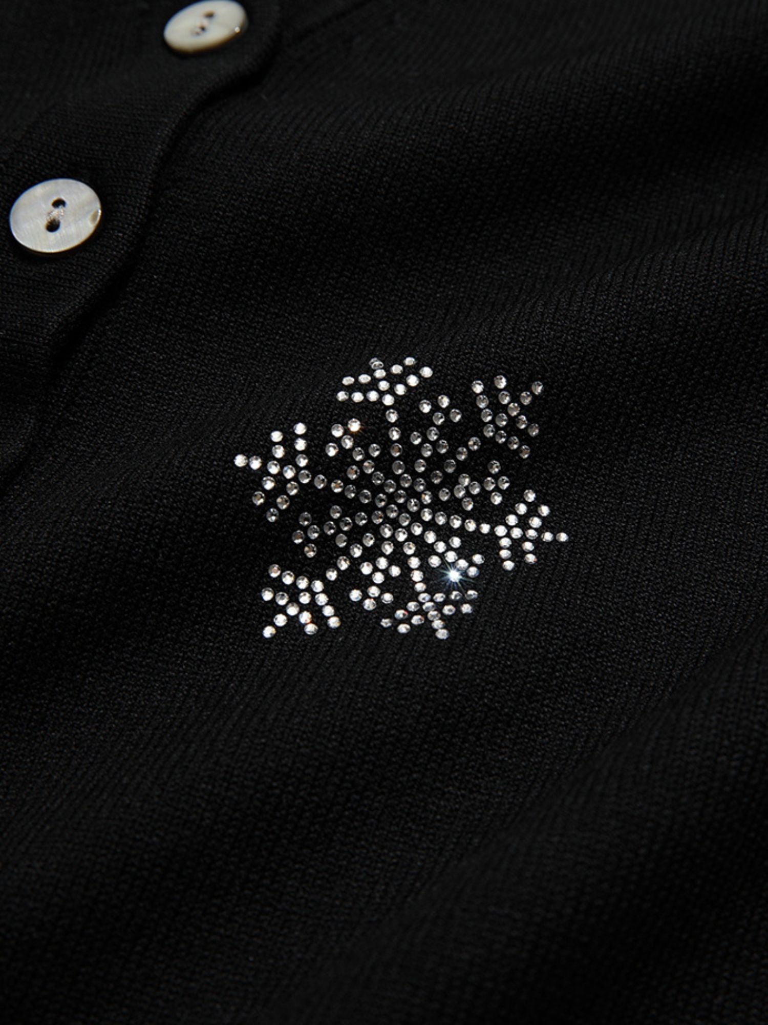 Detail view of snowflake embroidery on the upper chest of a black buttoned cardigan.