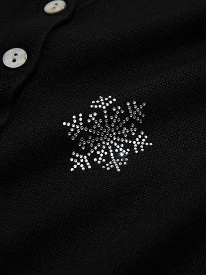 Detail view of snowflake embroidery on the upper chest of a black buttoned cardigan.