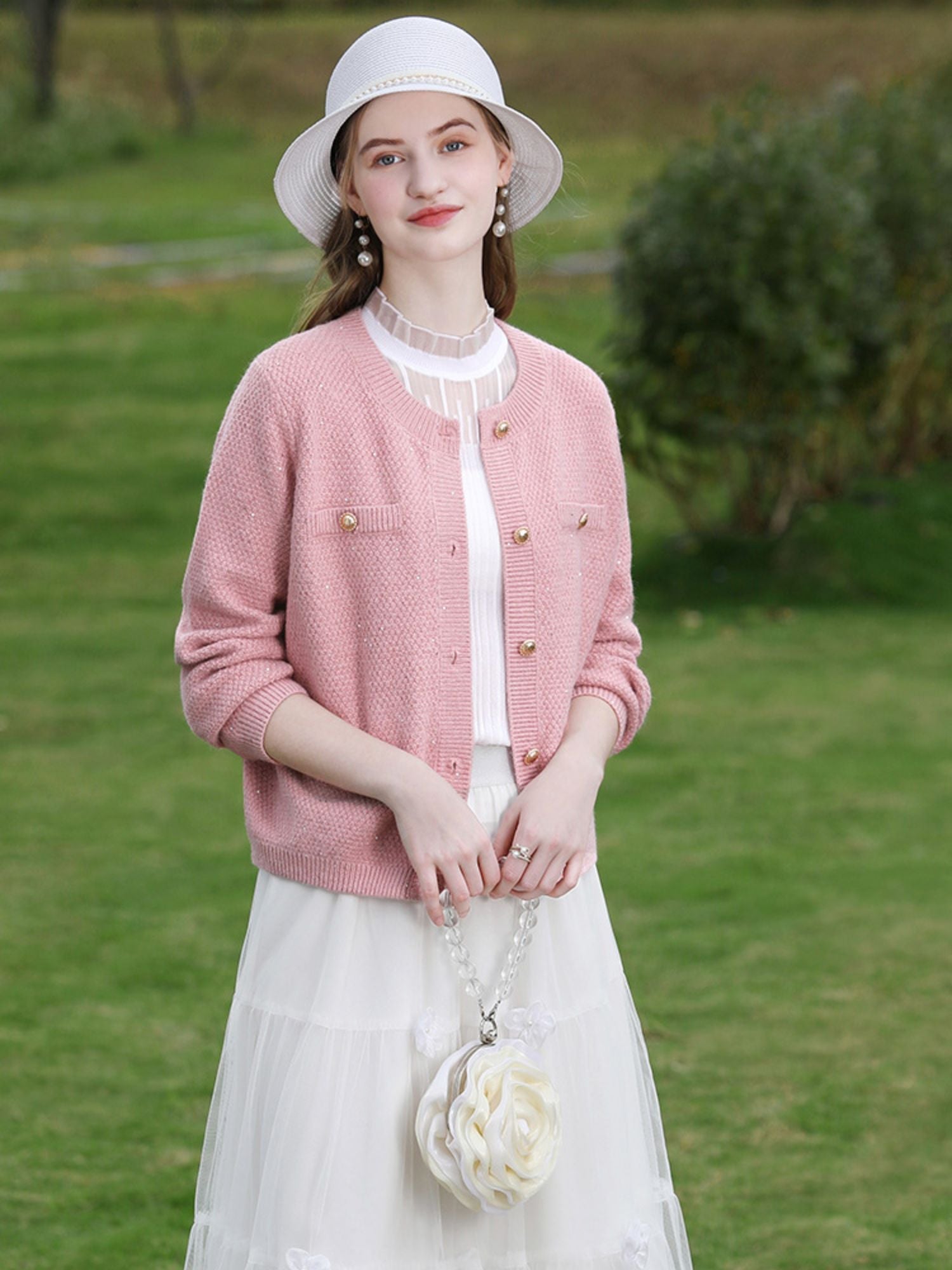Side view of woman in pink knit cardigan and white floral dress walking past flowers.