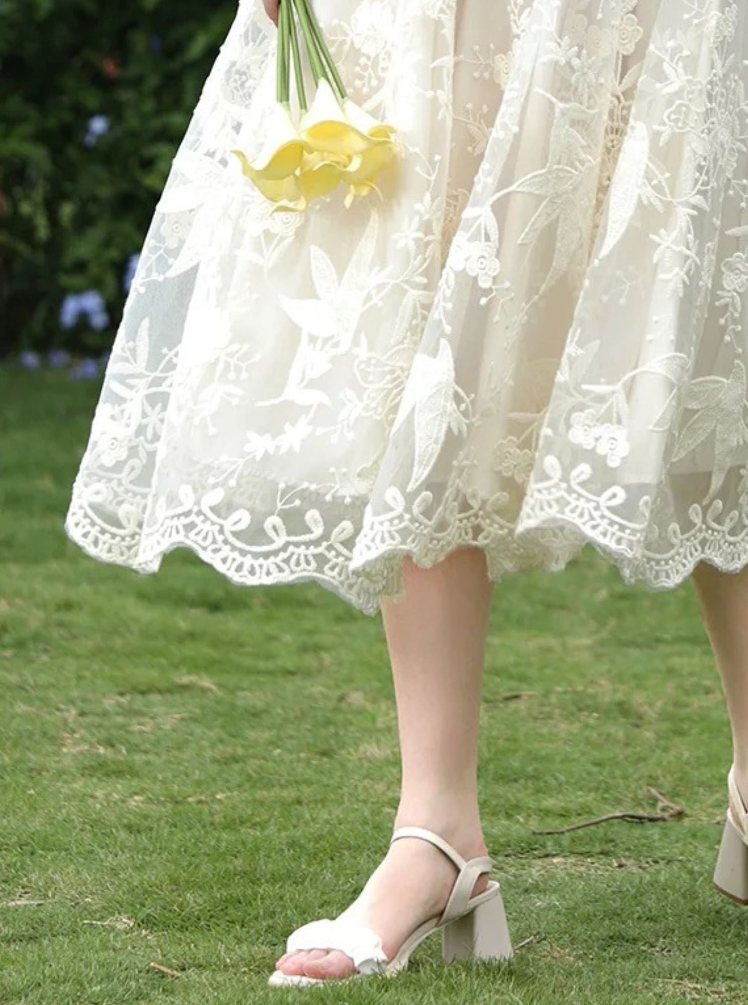 Side view of lace-trimmed midi skirt and strappy heels on grass.

