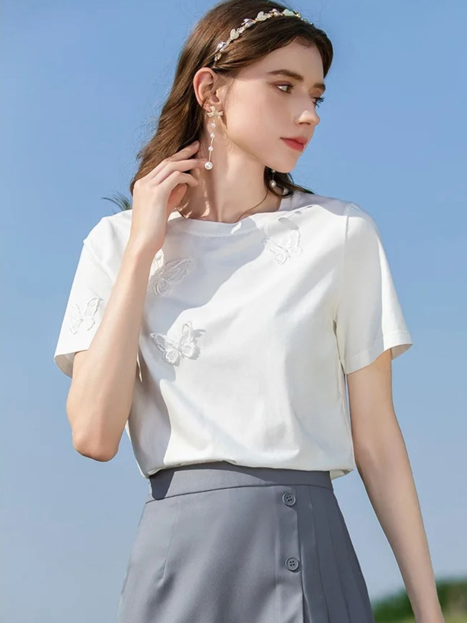 Front view of woman in white tee with butterfly embroidery, looking slightly down.