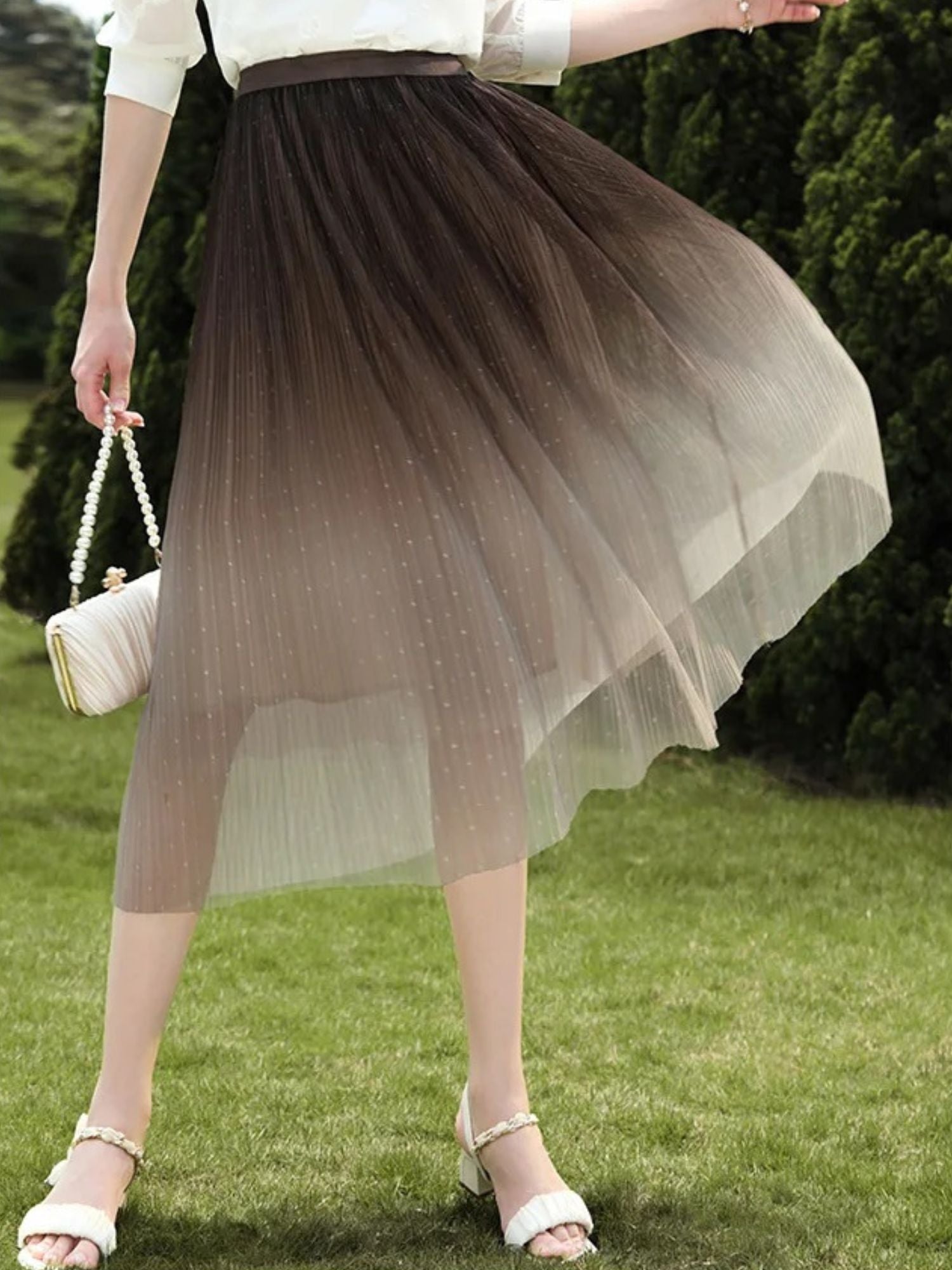 Back view of woman in gradient tulle skirt walking on grass in summer light.

