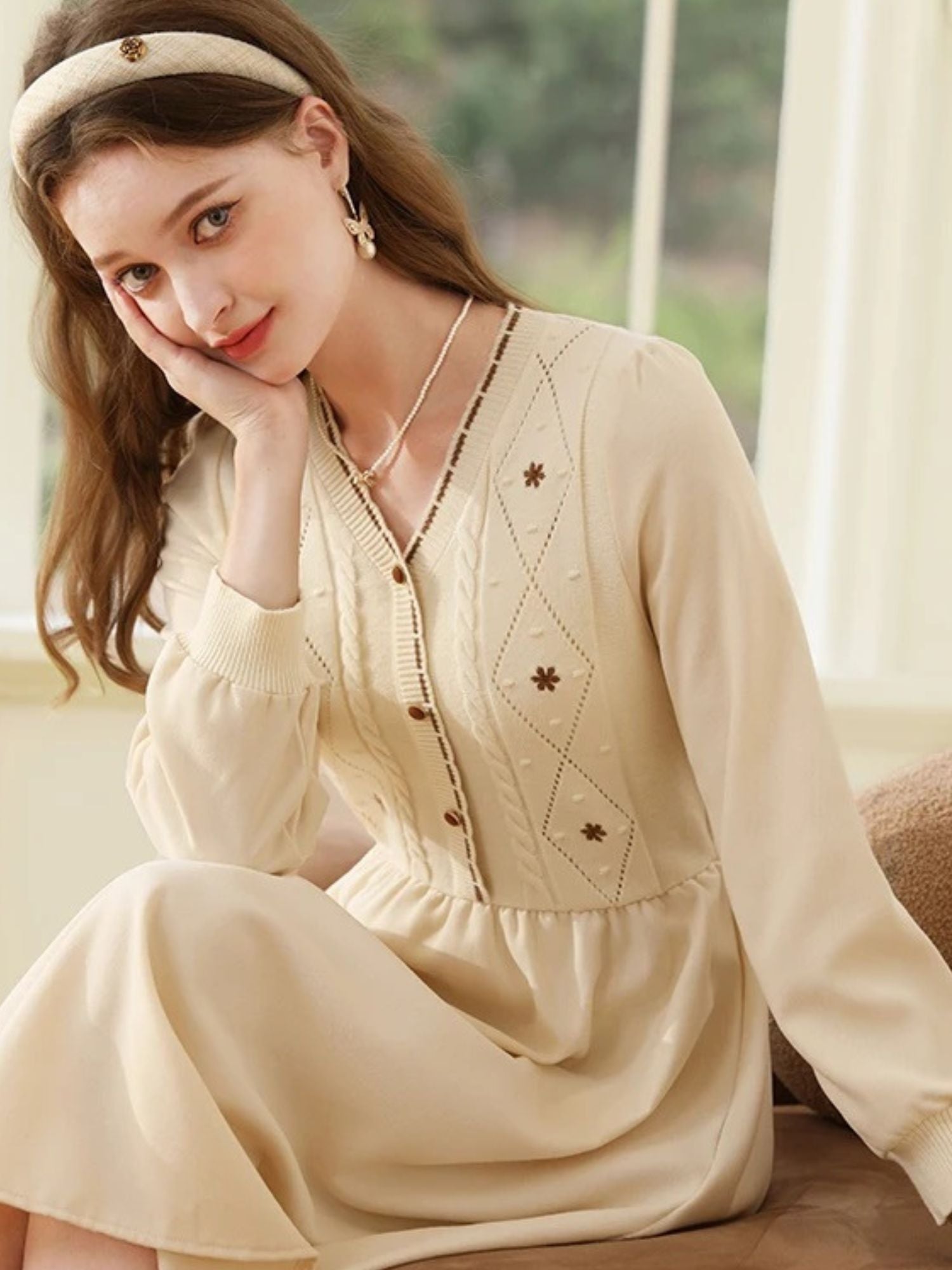 Woman sitting in cream dress, lifting the hem slightly to cross her legs.