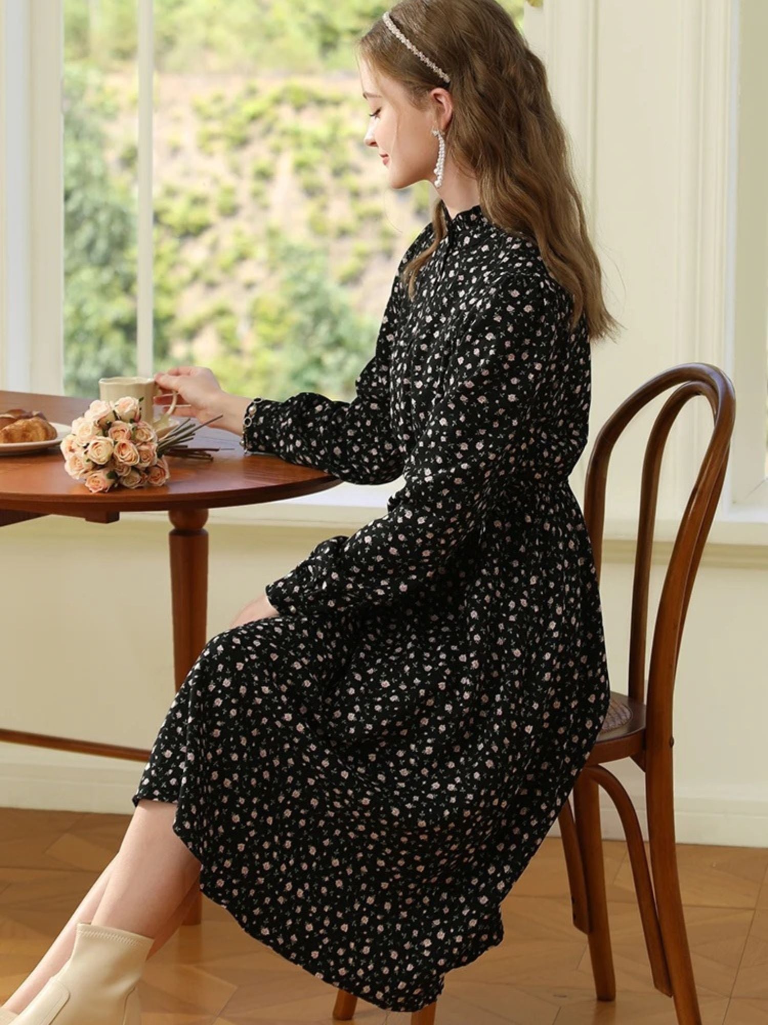 Seated woman in black floral dress looking down while resting her arm on a table.