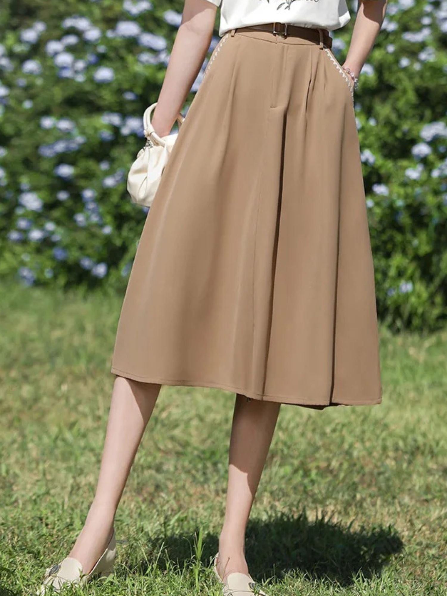 Side view of woman in brown midi skirt holding a cream handbag.