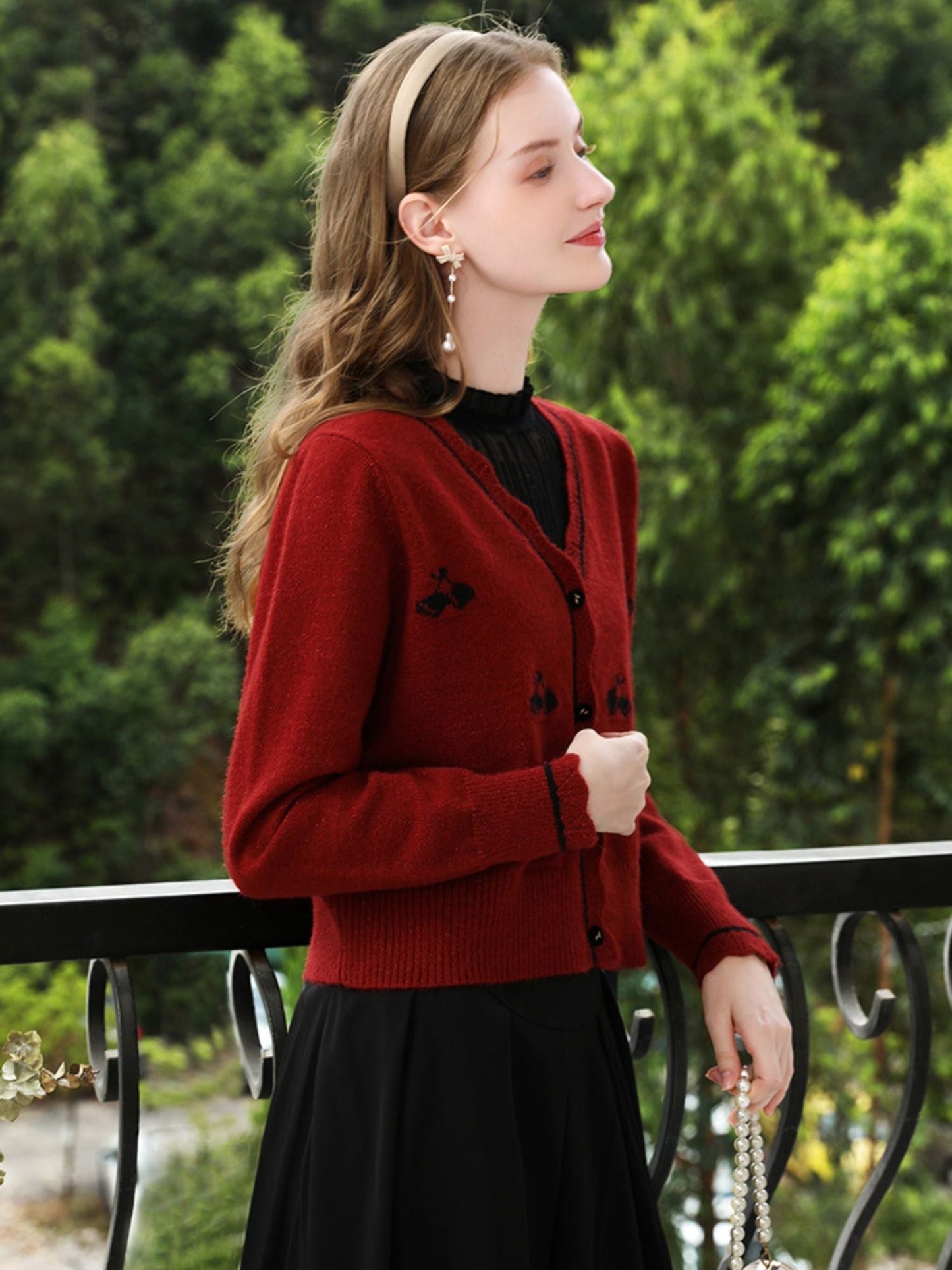 Woman smiling in red cardigan with puff sleeves, standing by greenery.